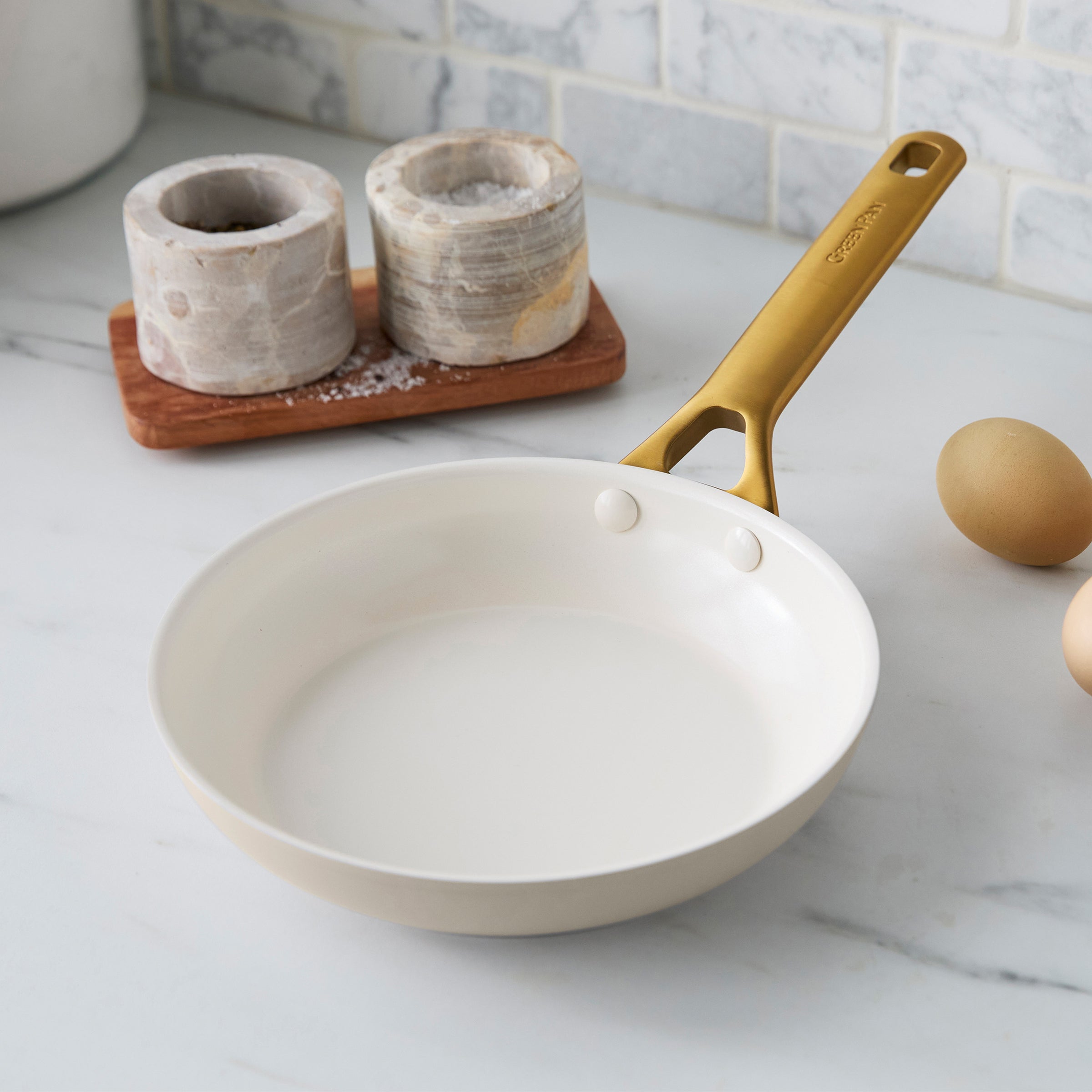 Taupe frying pan with gold handle on a kitchen counter
