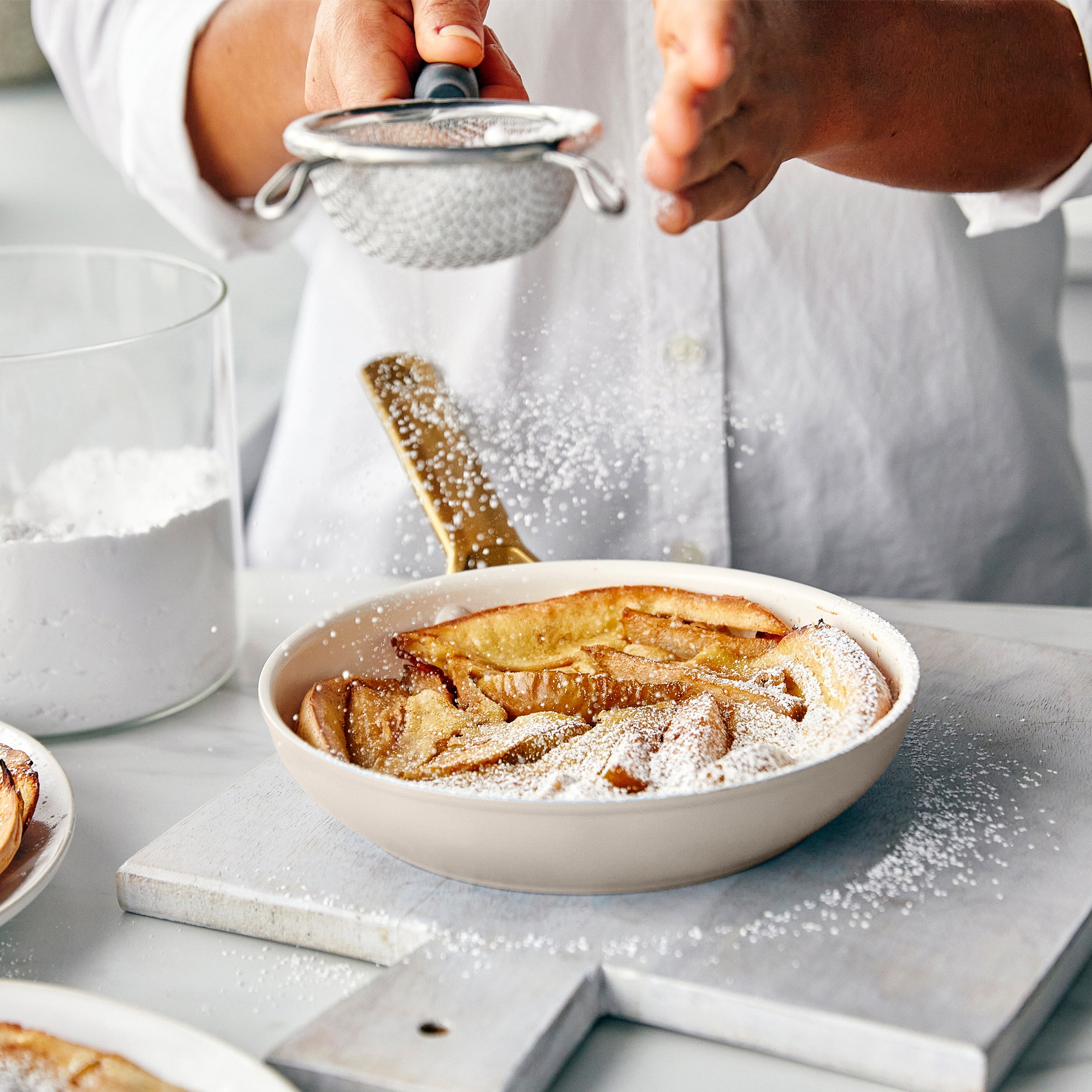 Person dusting a dish of apple pie with powdered sugar using a sifter.