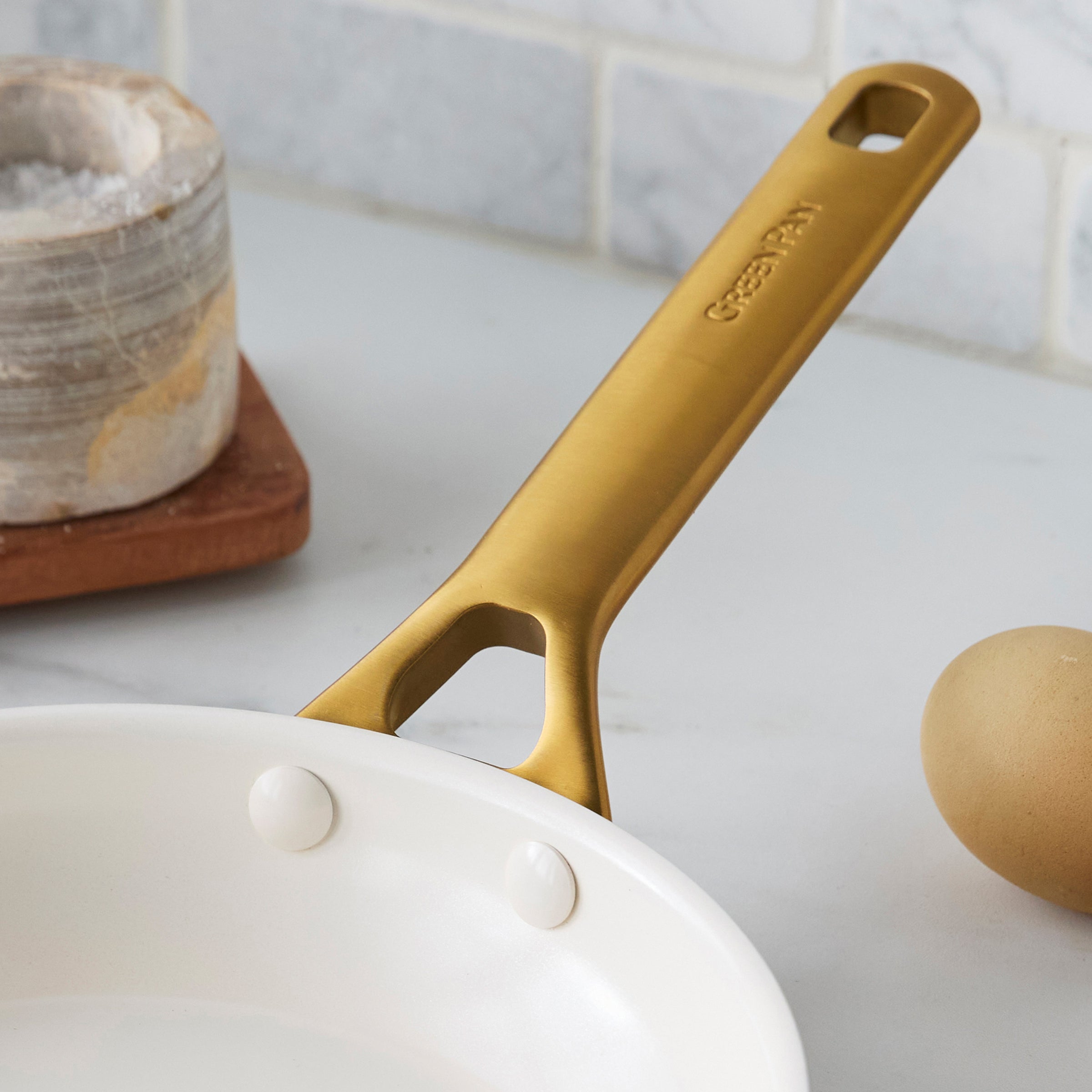 Taupe frying pan with a gold handle on a kitchen counter.