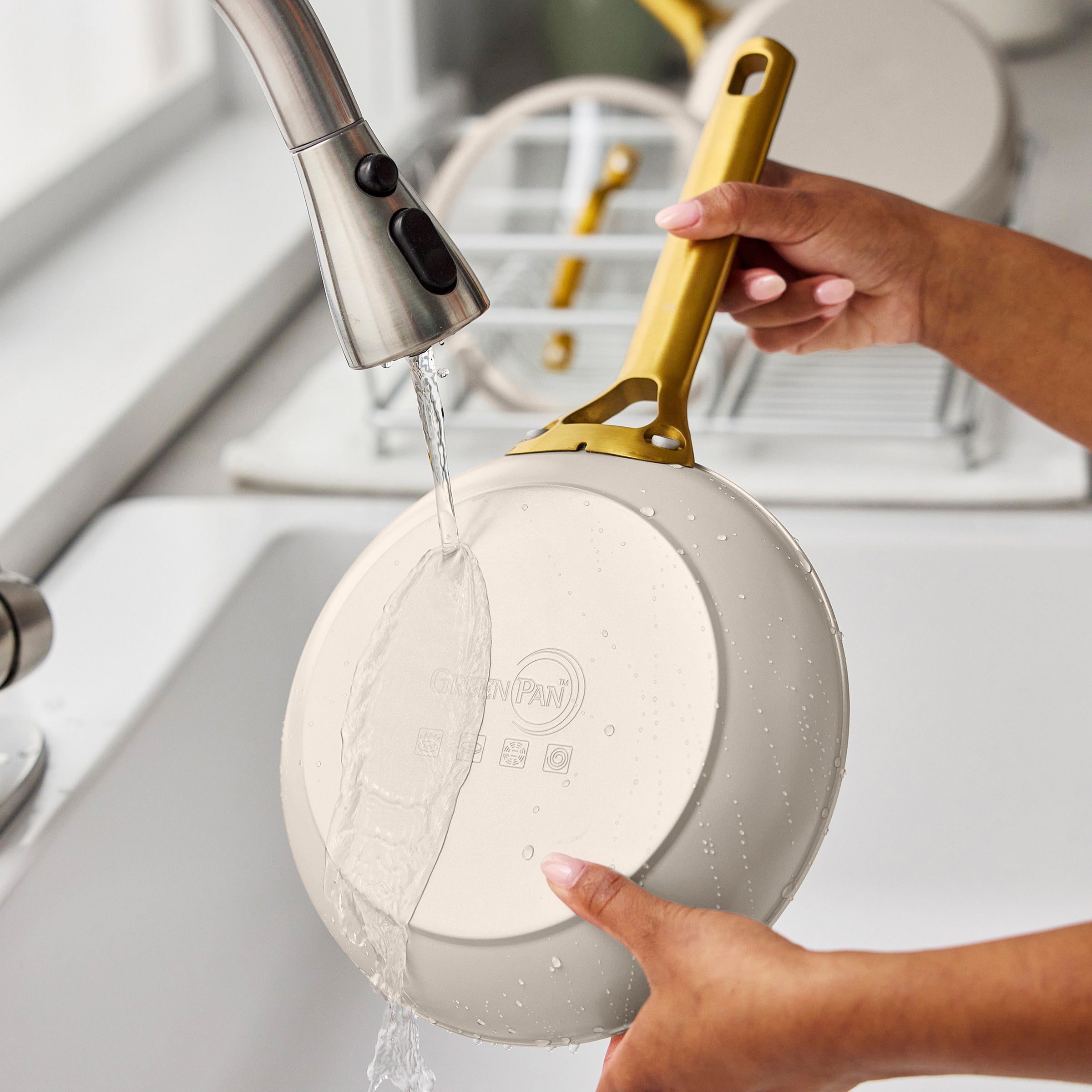 Person washing a taupe frying pan with a gold handle in a kitchen sink