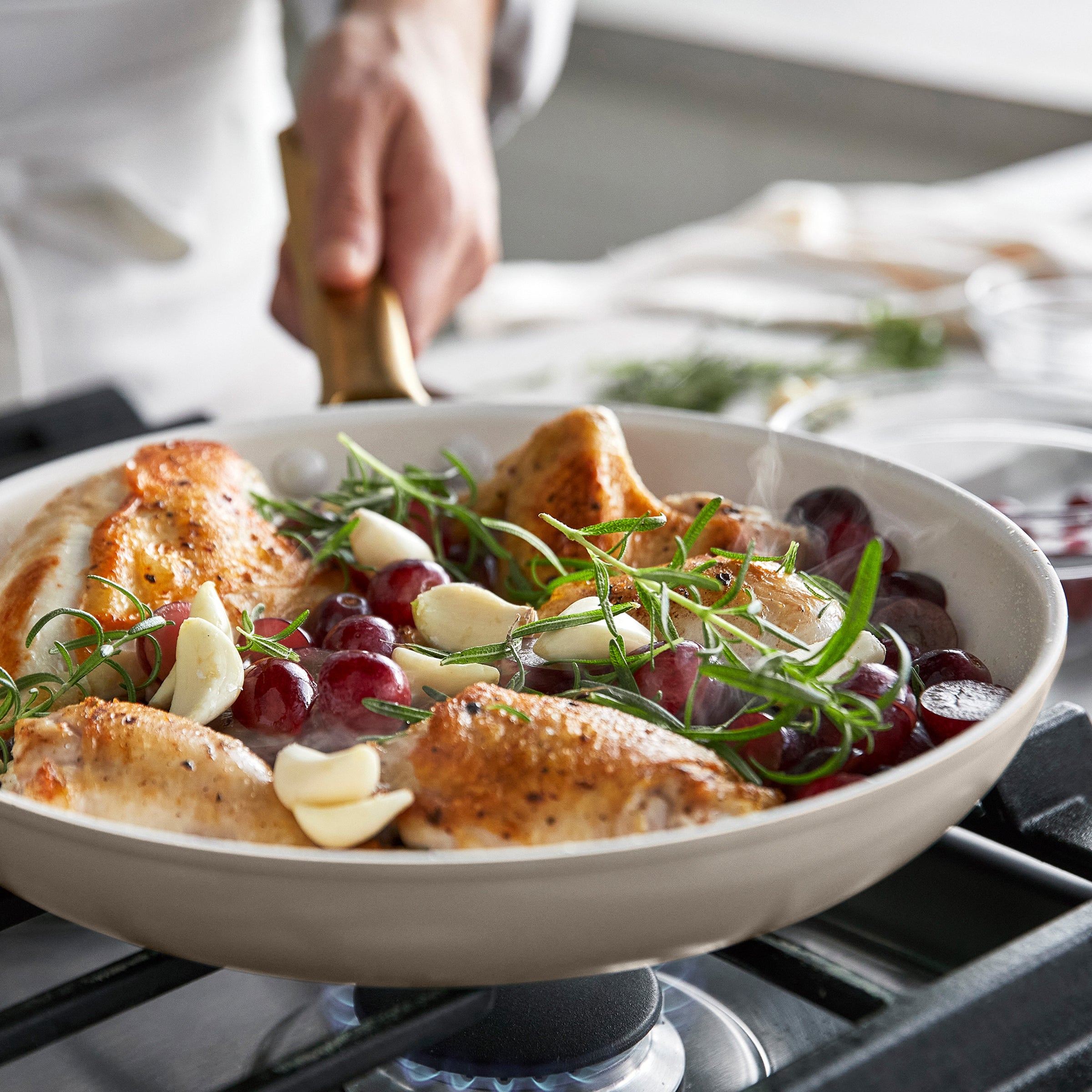 Roasted chicken with grapes and herbs in a taupe frypan on a stove