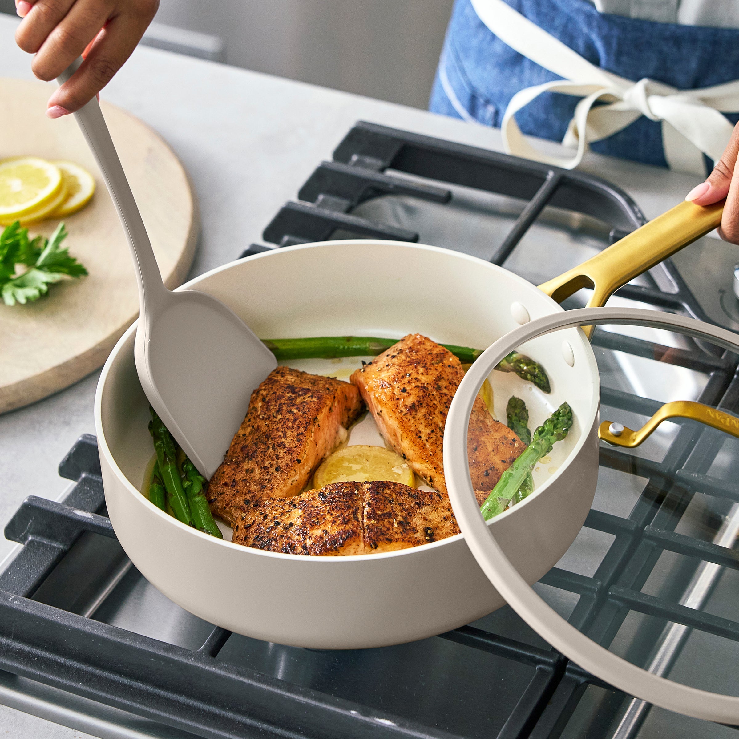 Person cooking salmon in a taupe saute pan on a stove with spatula