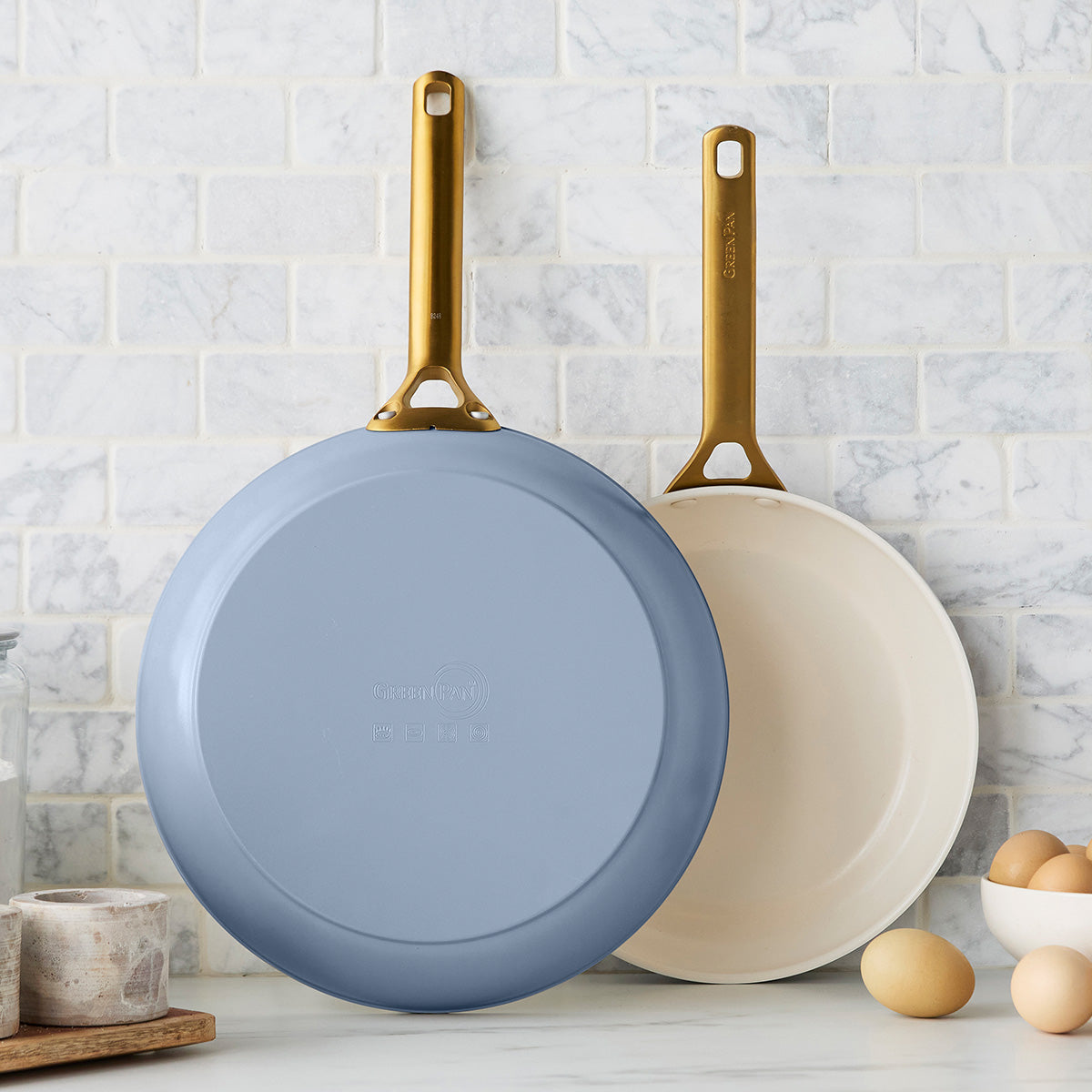Two blue frying pans with gold handles on a kitchen counter.