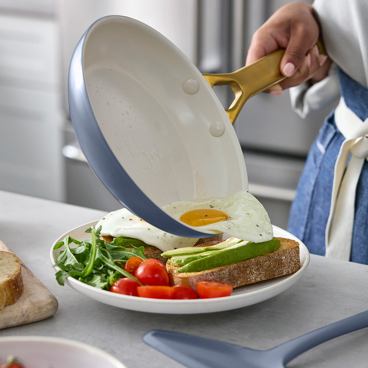 Person using a blue frying pan to place an egg on a plate with toast and avocado.