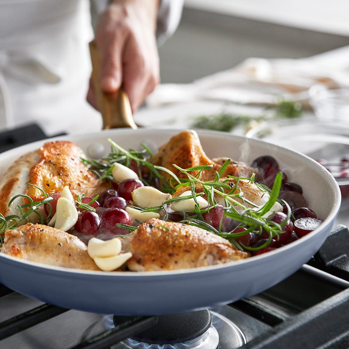 Roasted chicken dish with grapes and herbs in a blue frypan on a stove.
