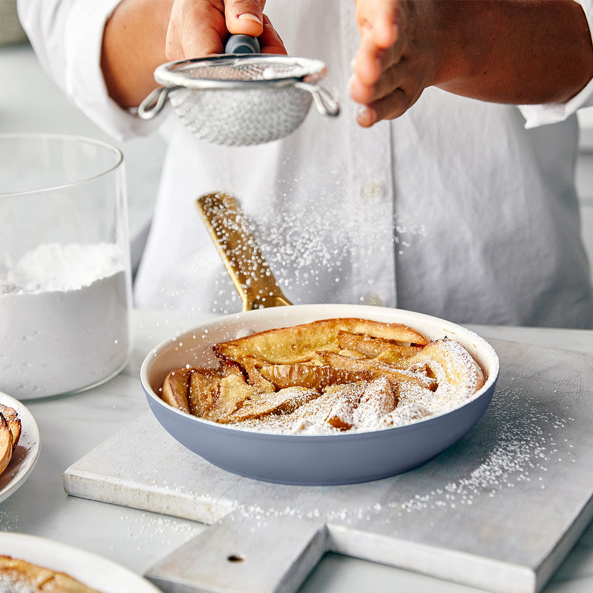 Person dusting a dish of apple slices with powdered sugar using a sifter.