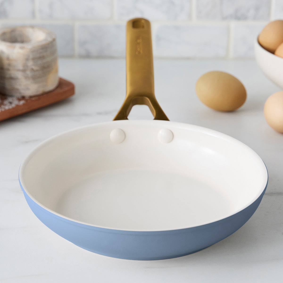 Blue frying pan with a gold handle on a kitchen counter.