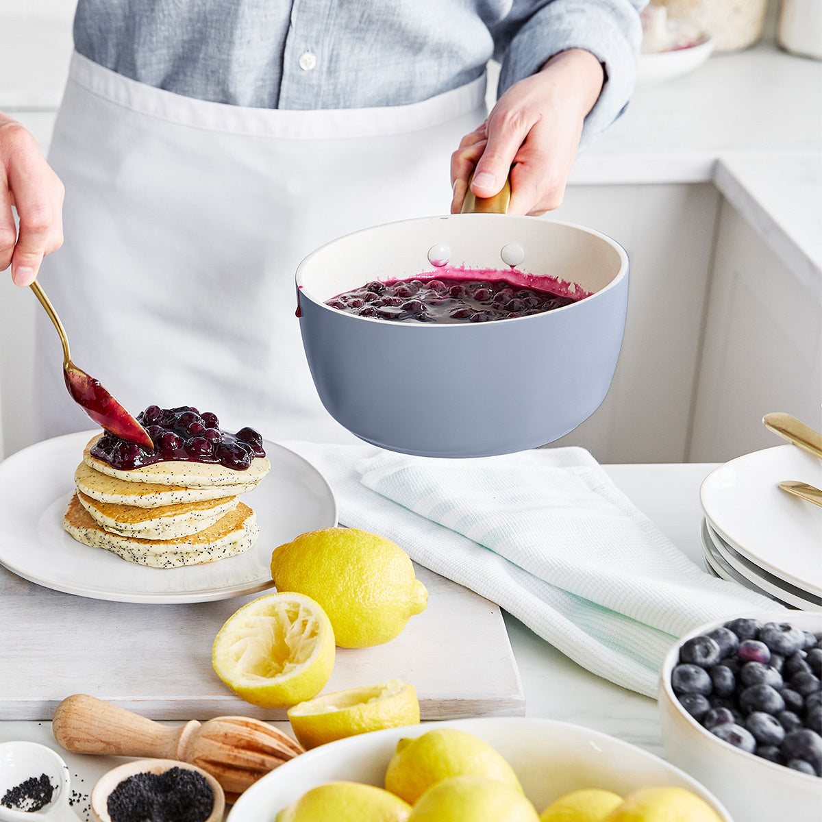 Person preparing pancakes with blueberry sauce in a kitchen setting