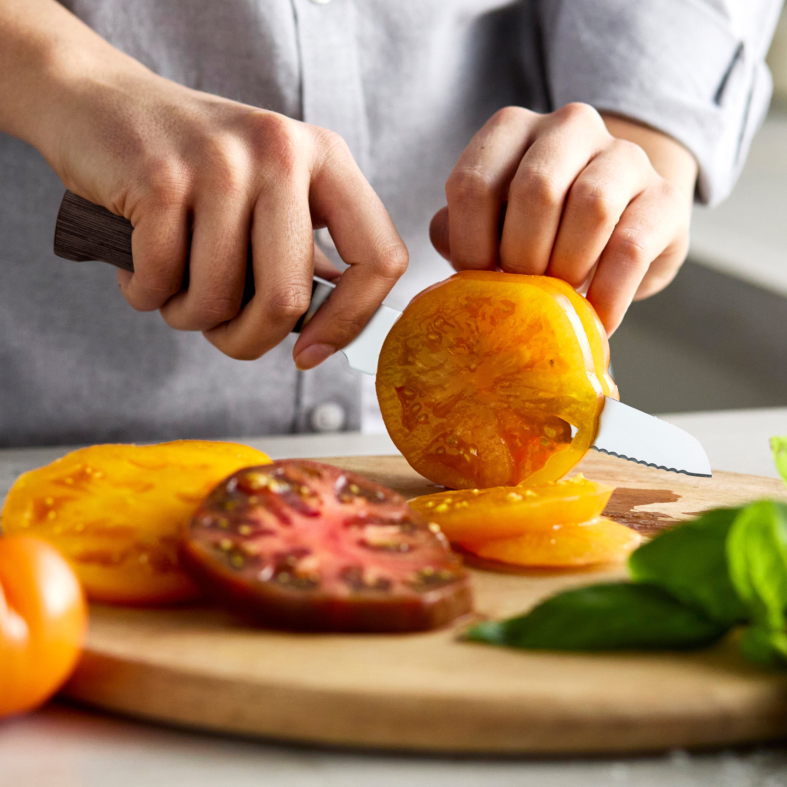 Person slicing tomatoes on a wooden cutting board with a knife.