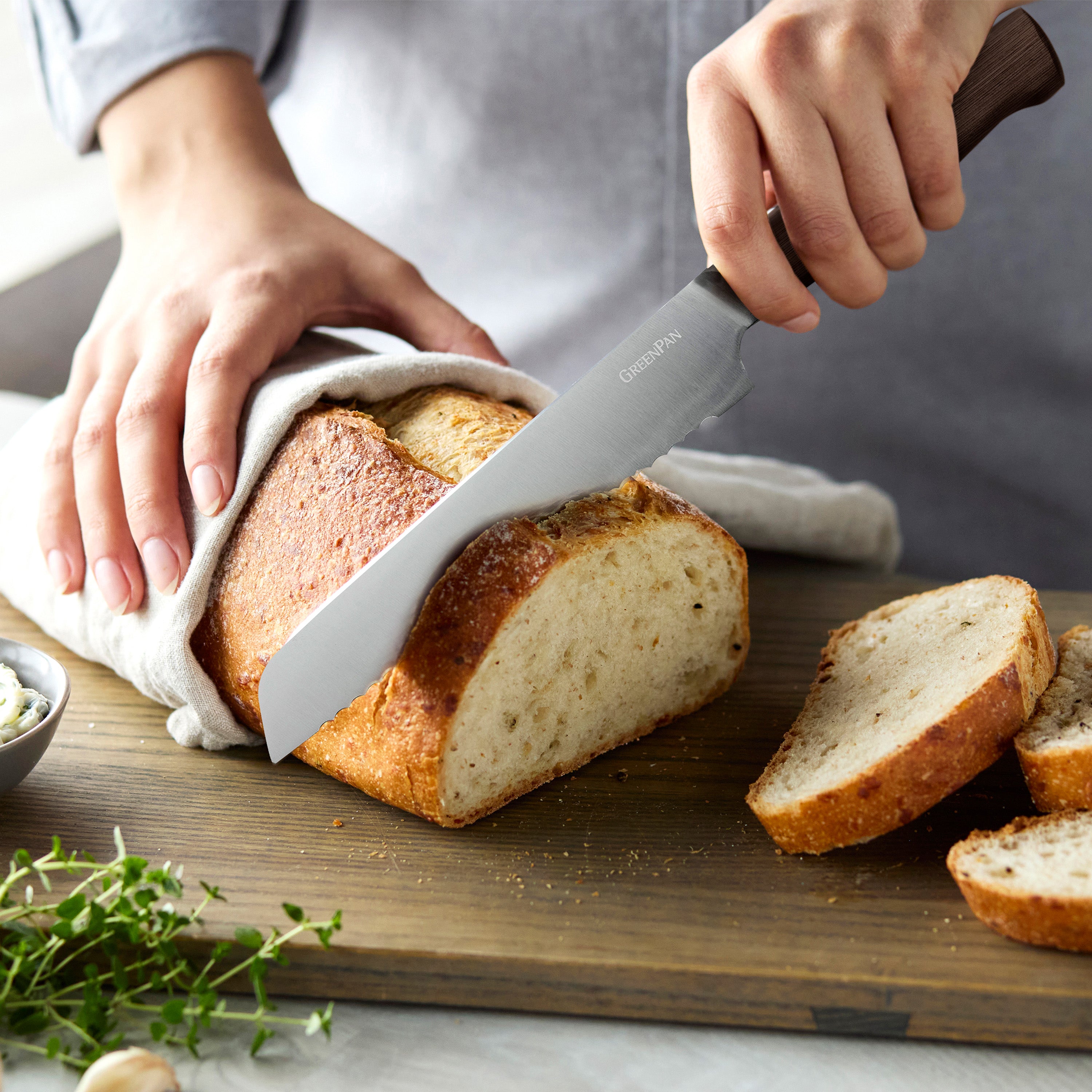 Person slicing bread with a knife on a wooden cutting board