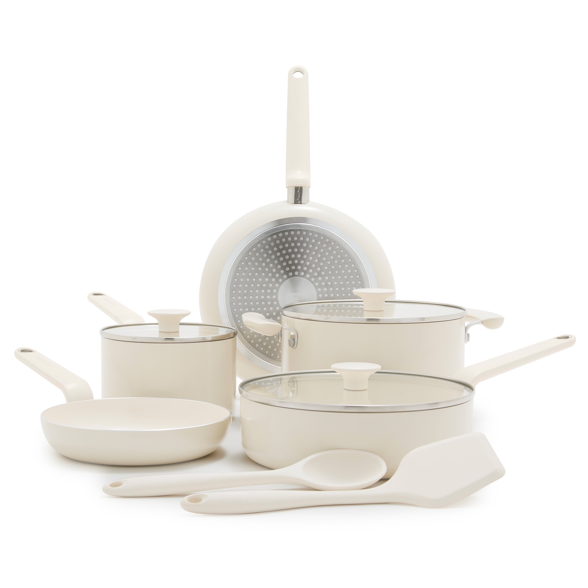 Cream ceramic 10-piece cookware set with pots, pans, glass lids, a spatula, and spoon arranged on a white background.