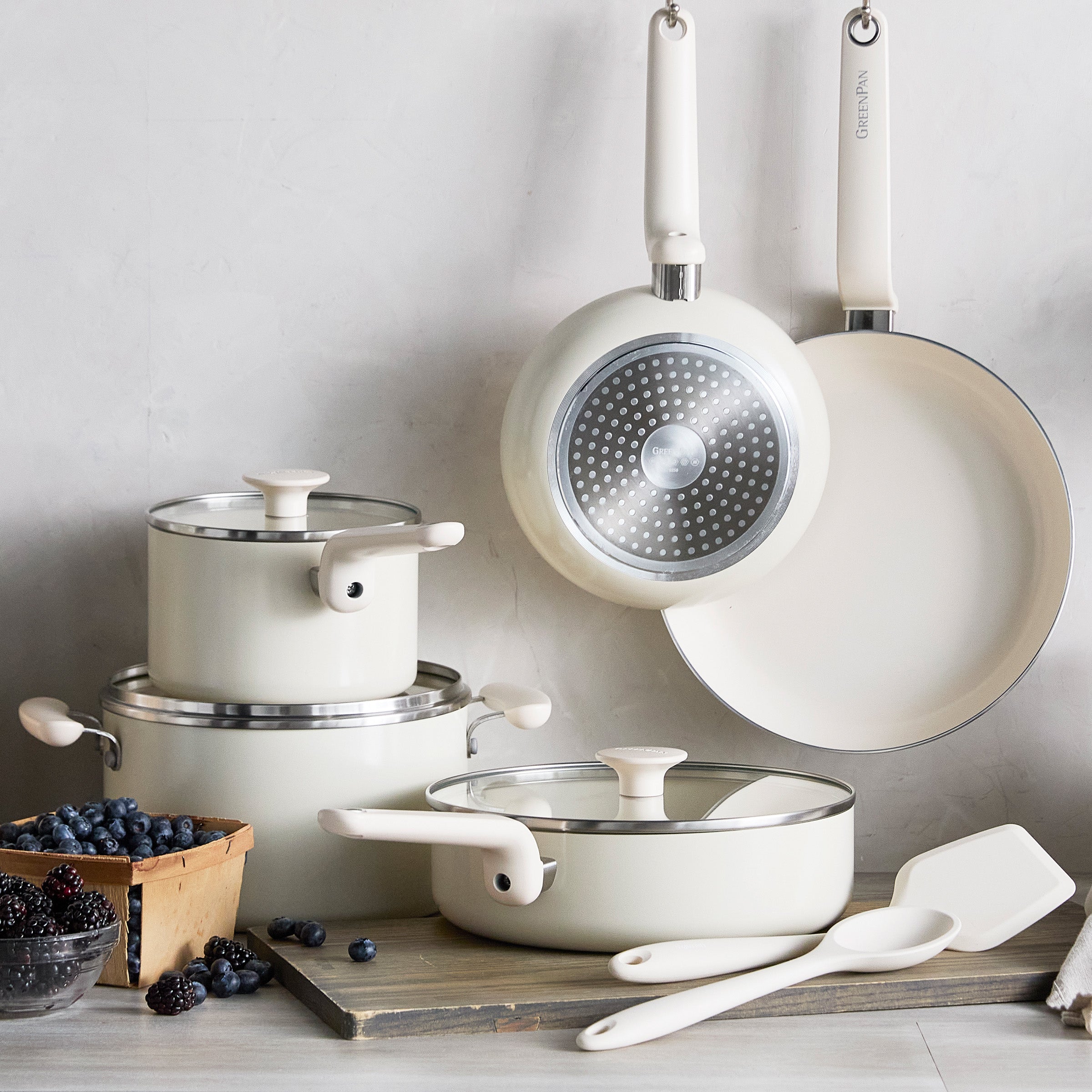 Cream ceramic 10-piece cookware set with utensils and blackberries on a wooden surface.
