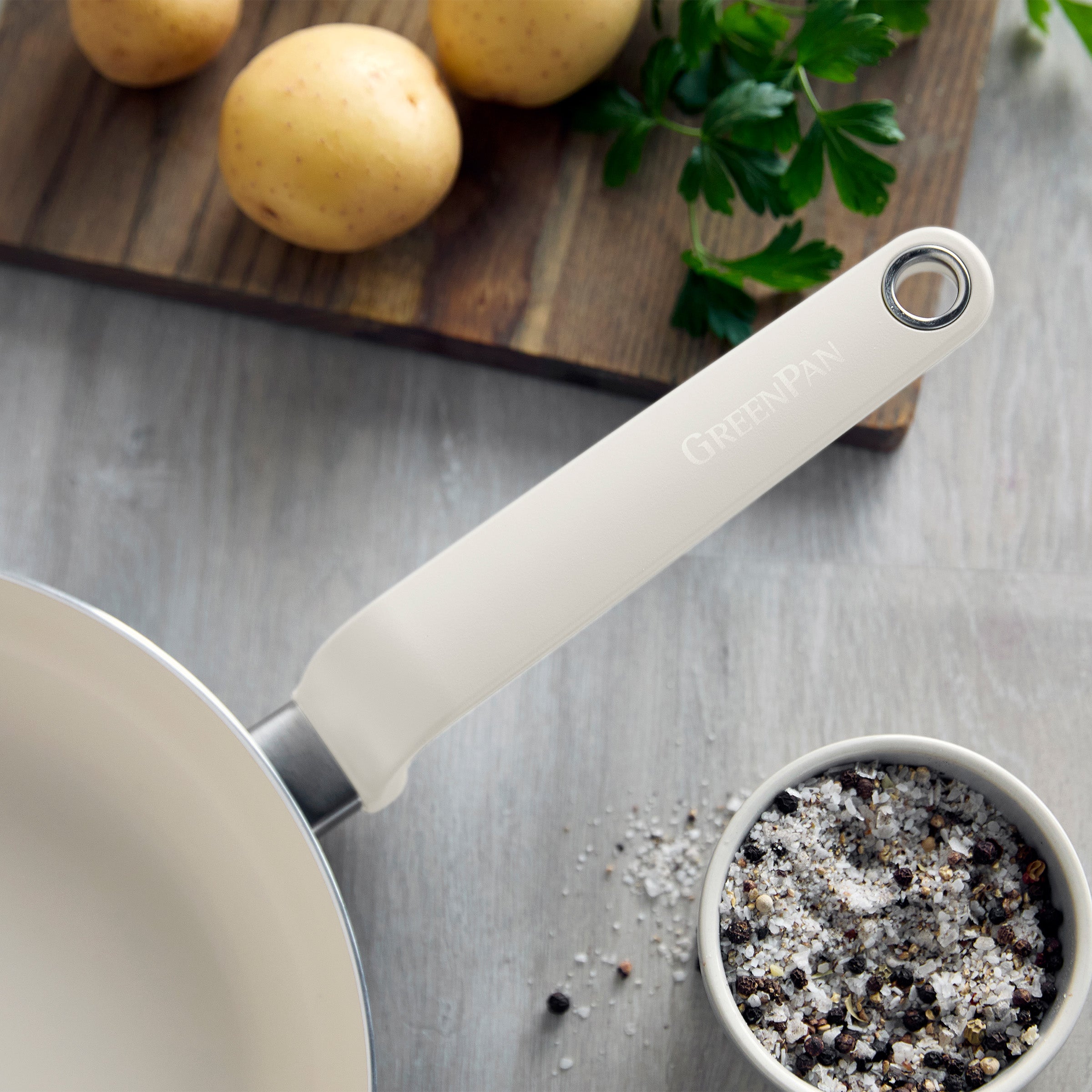 Cream ceramic 10-piece cookware set with white handles, shown with whole potatoes on a light wooden board.