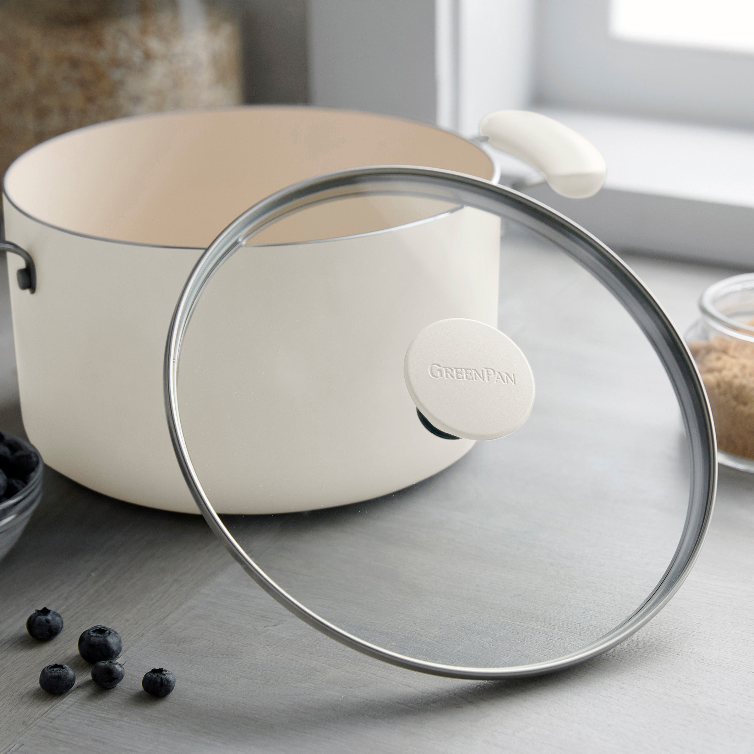 Cream ceramic nonstick 10-piece cookware set on a counter with blueberries and brown sugar nearby.