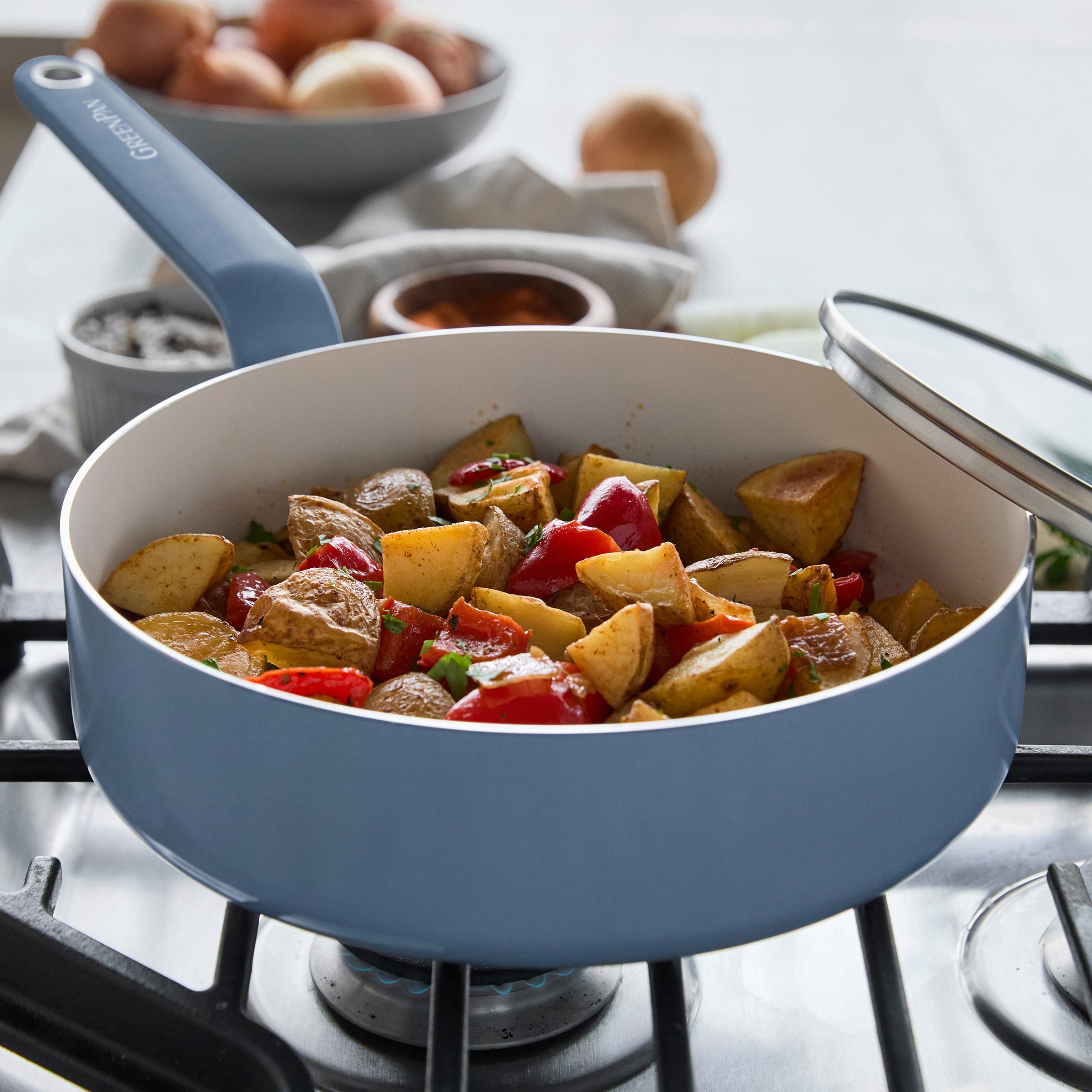Blue ceramic nonstick saucepan from 10-piece set, with roasted potatoes, peppers, onions, and spices placed nearby.