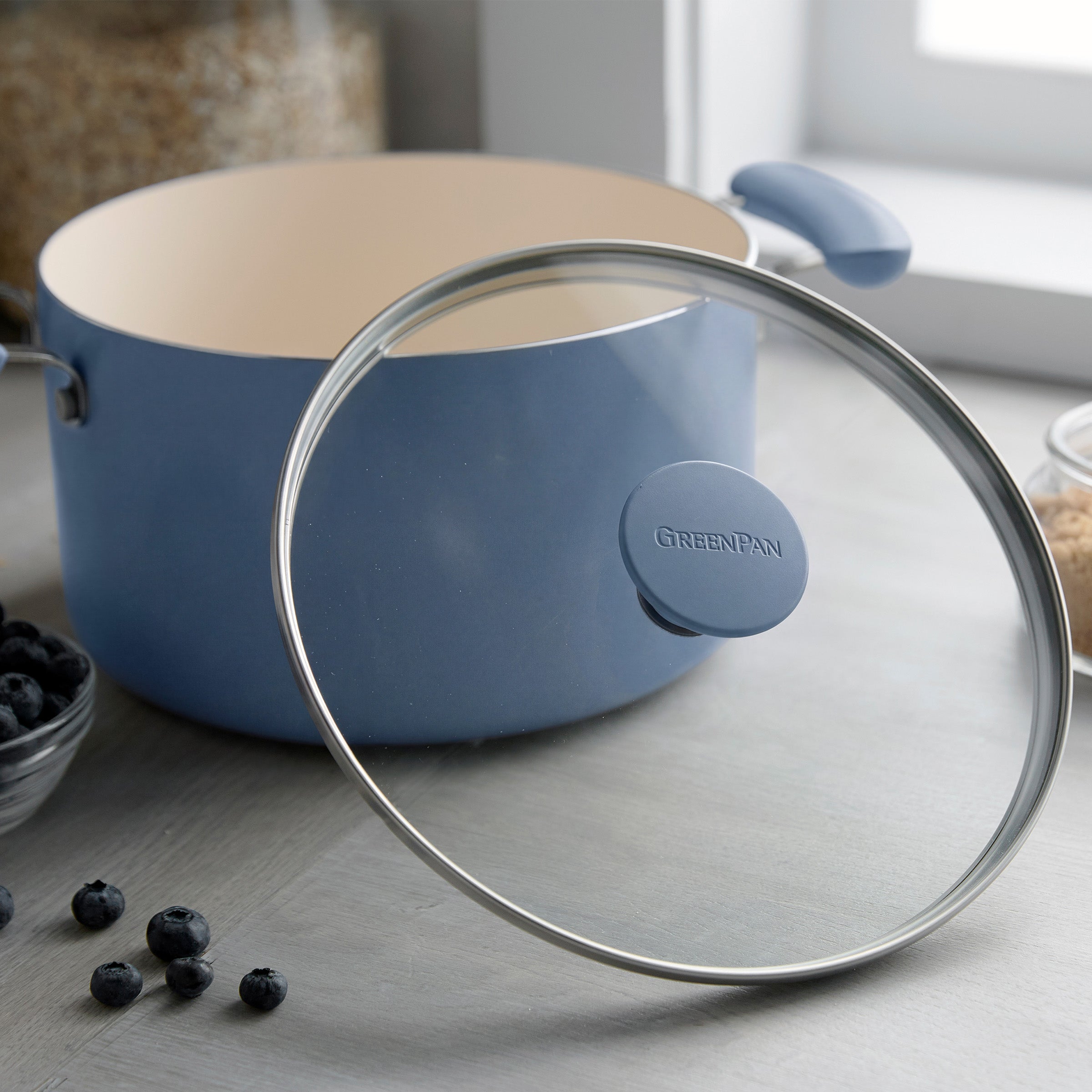Dutch blue ceramic cookware set on a gray counter next to jars of grains and a bowl of blueberries.