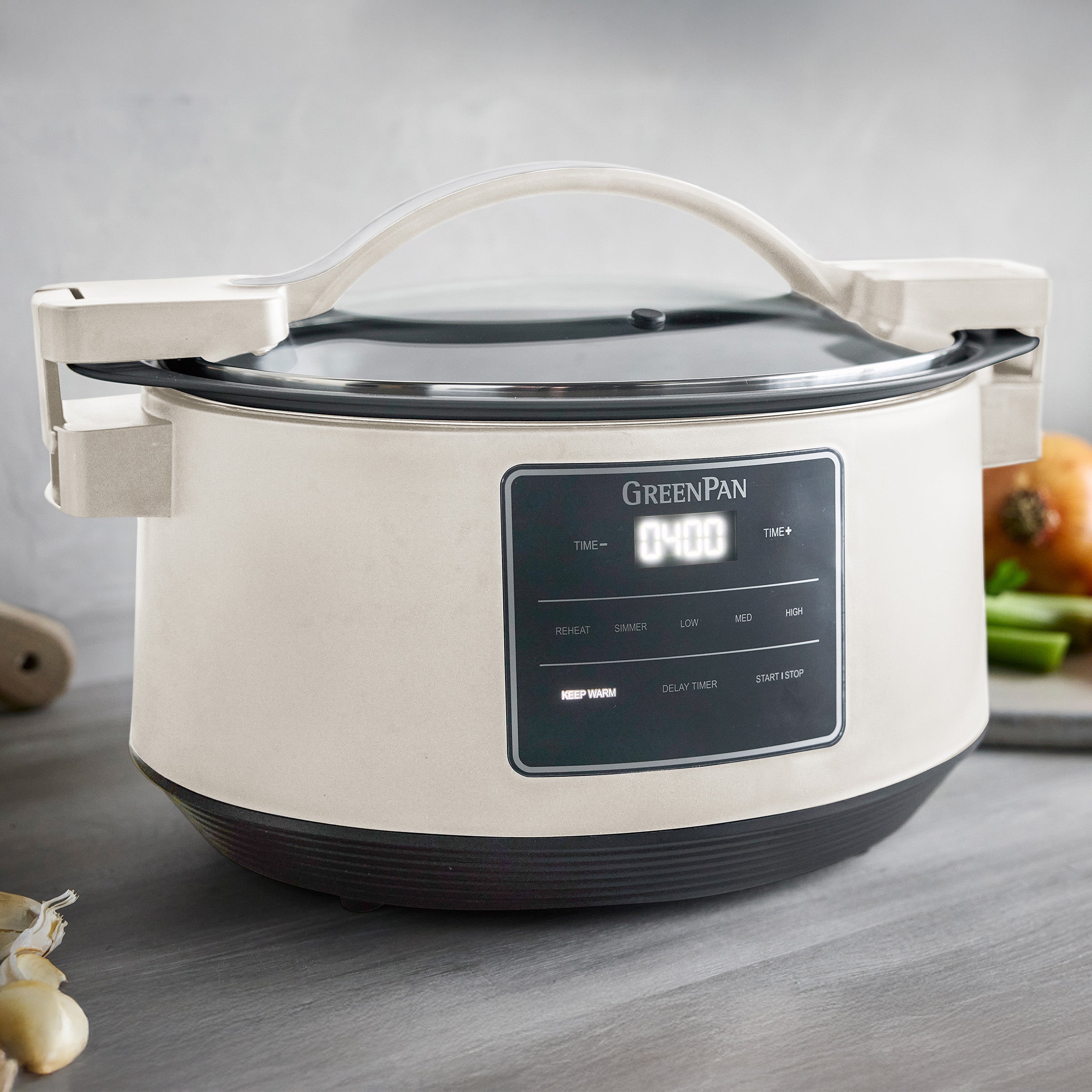 White GreenPan slow cooker on a wooden surface with vegetables in the background
