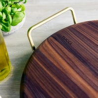 Wooden pizza stone with gold handle on a light surface, featuring the brand 'Tucci'.