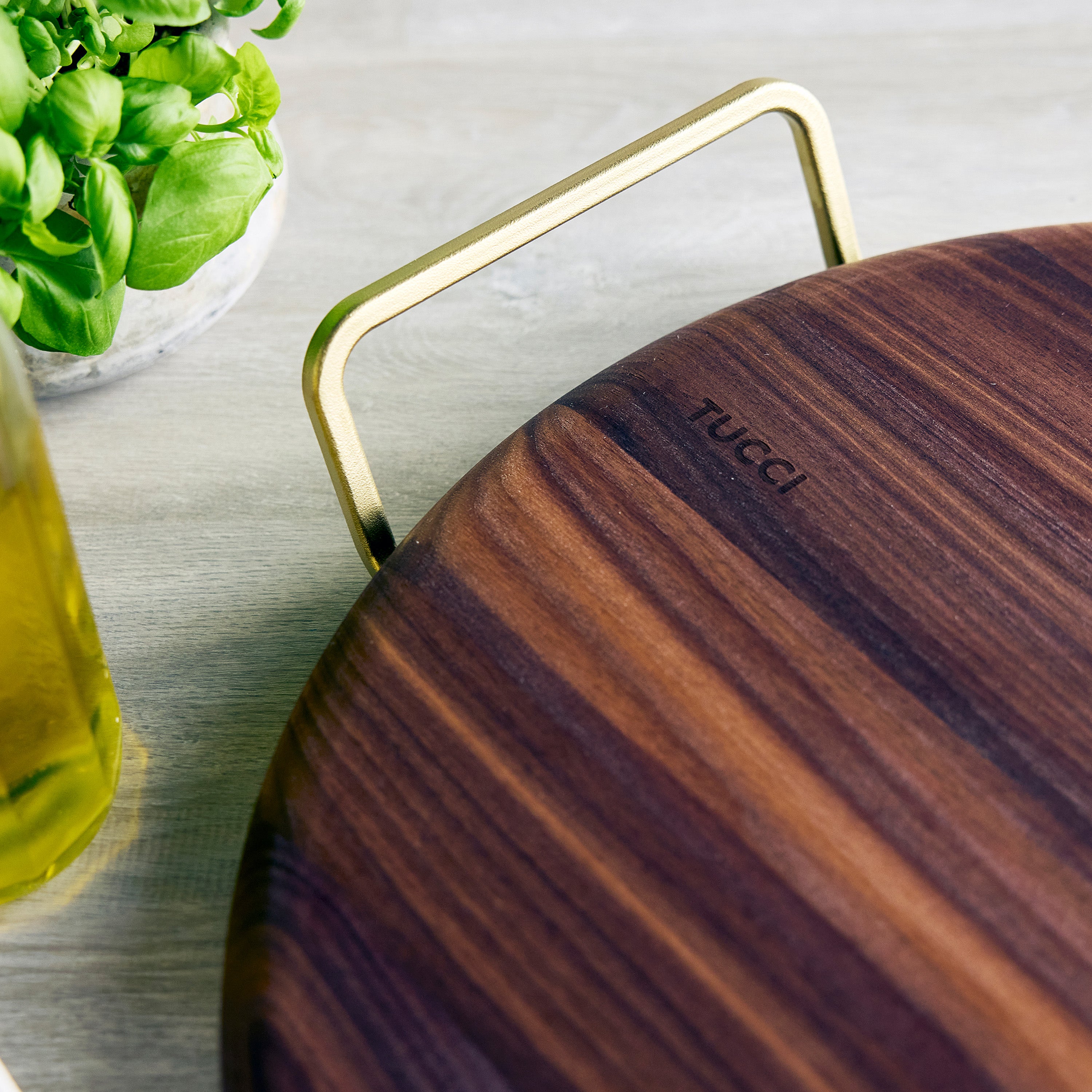 Wooden pizza stone with gold handle on a light surface, featuring the brand 'Tucci'.
