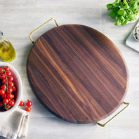 Wooden pizza stone with a handle on a light surface with vegetables and a bottle of oil.