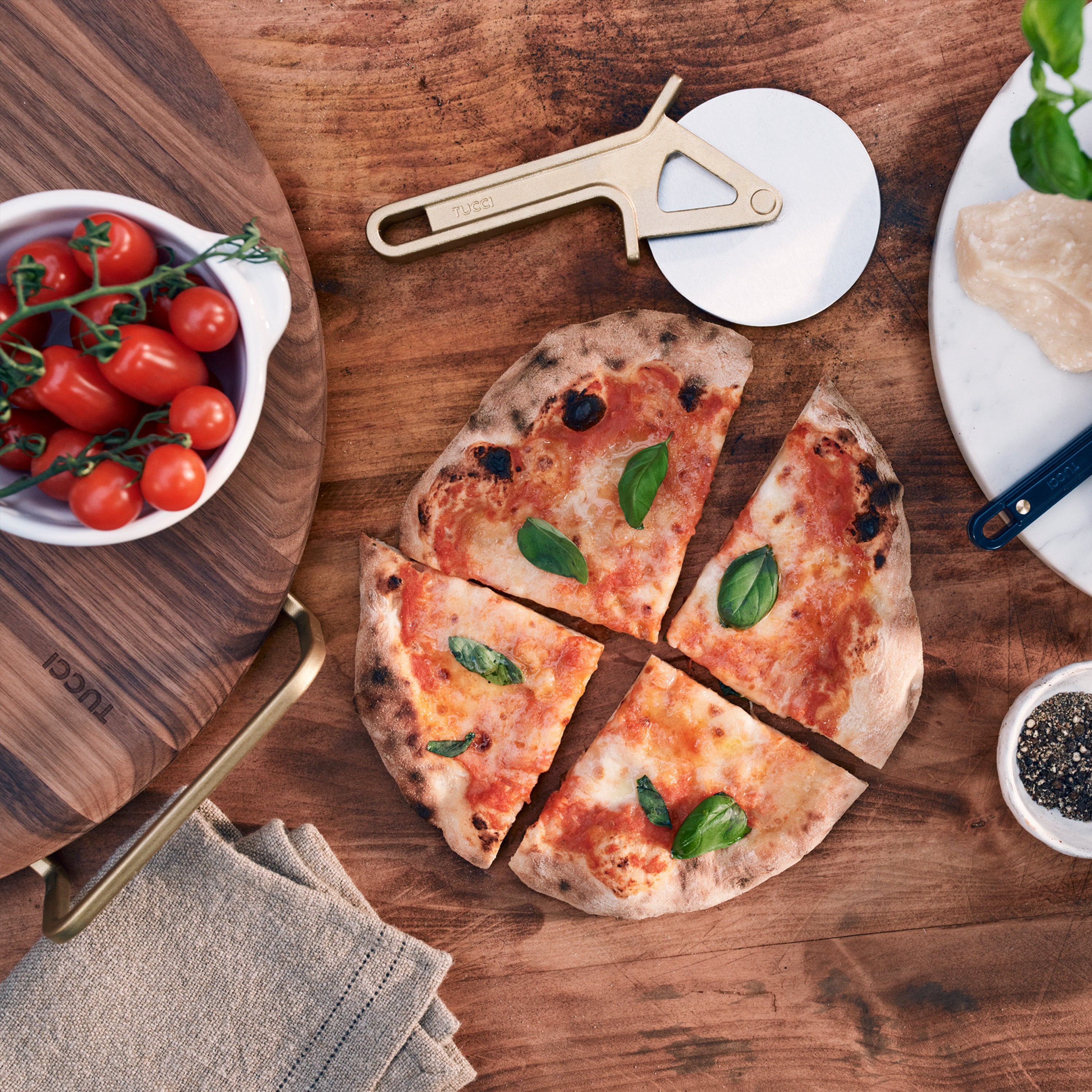 Wooden pizza stone with a small pizza, tomatoes, and a pizza cutter.