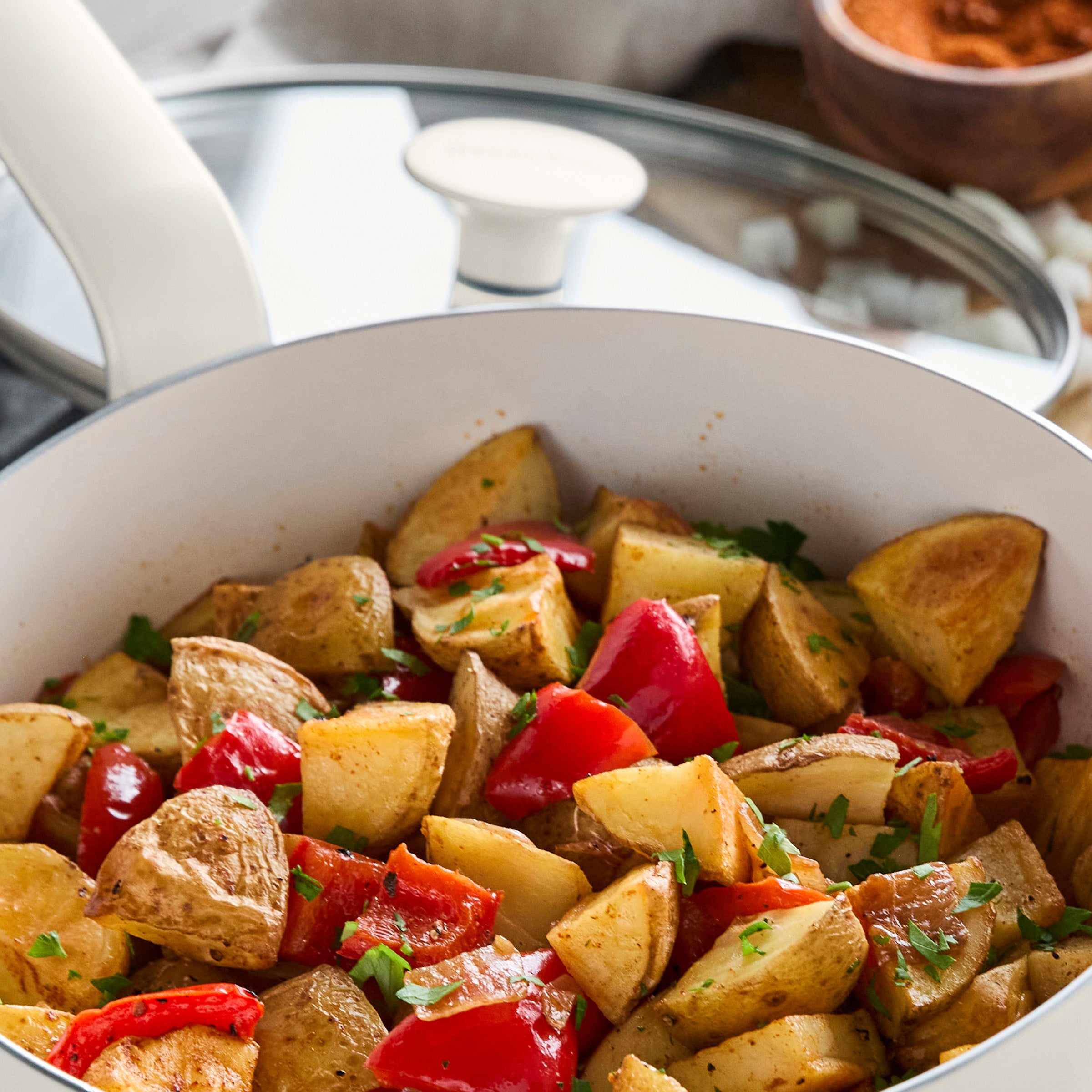Cream ceramic sauté pan with lid holding roasted potatoes and peppers, garnished with parsley, 5-quart capacity.