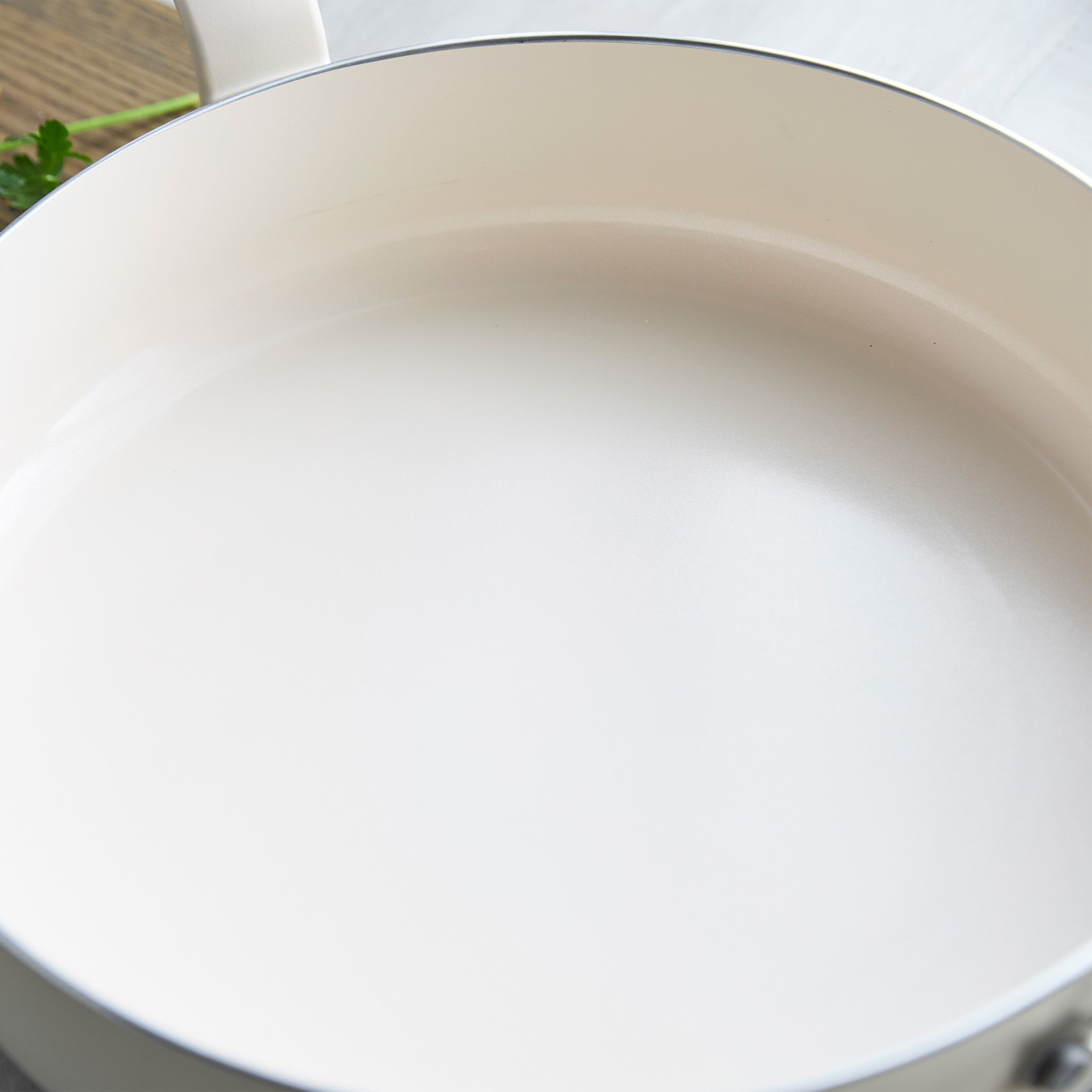 Cream ceramic nonstick 5-quart sauté pan with matching lid shown empty on a light surface.
