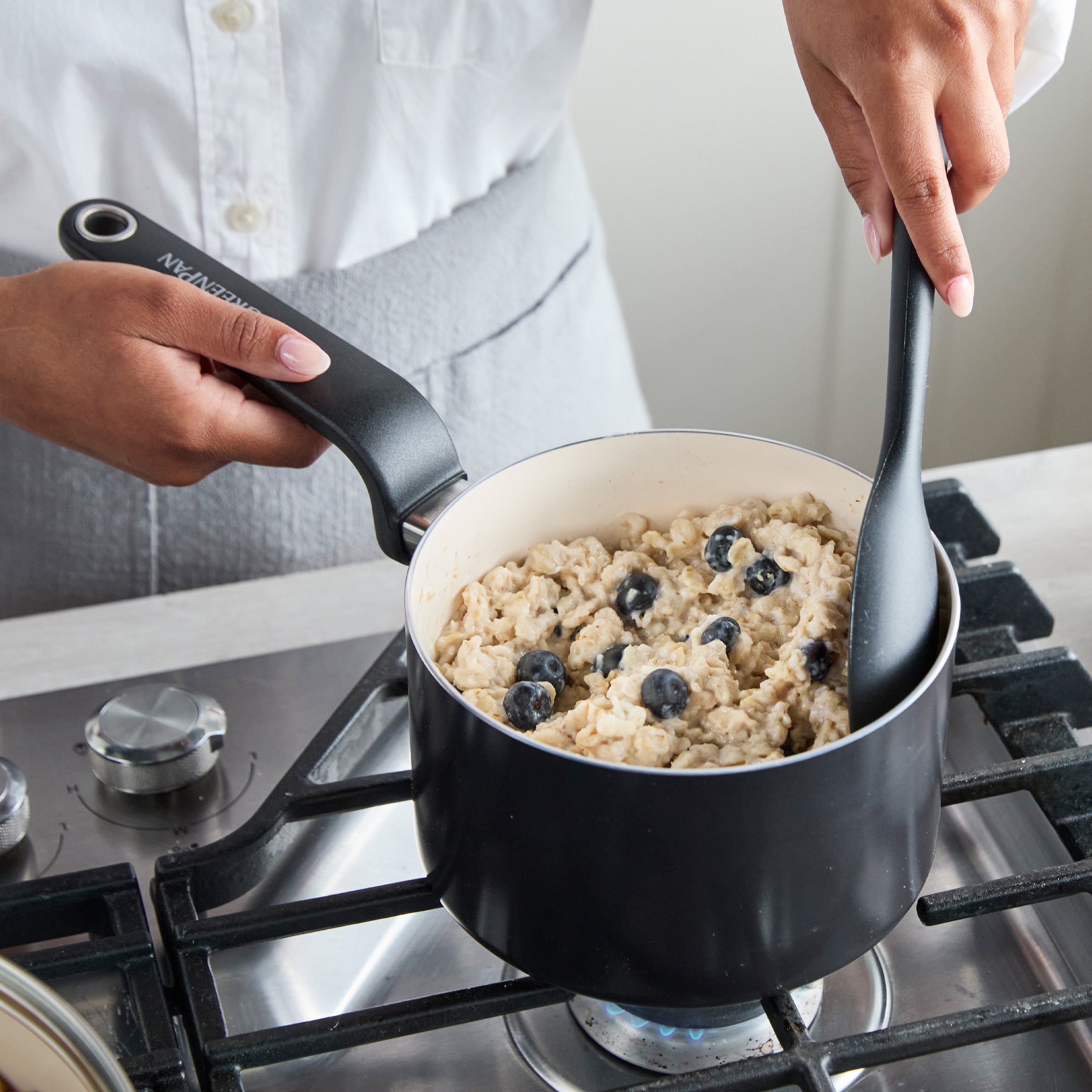 Blueberry oatmeal being stirred in a black ceramic nonstick 2-quart saucepan with lid on a stovetop.