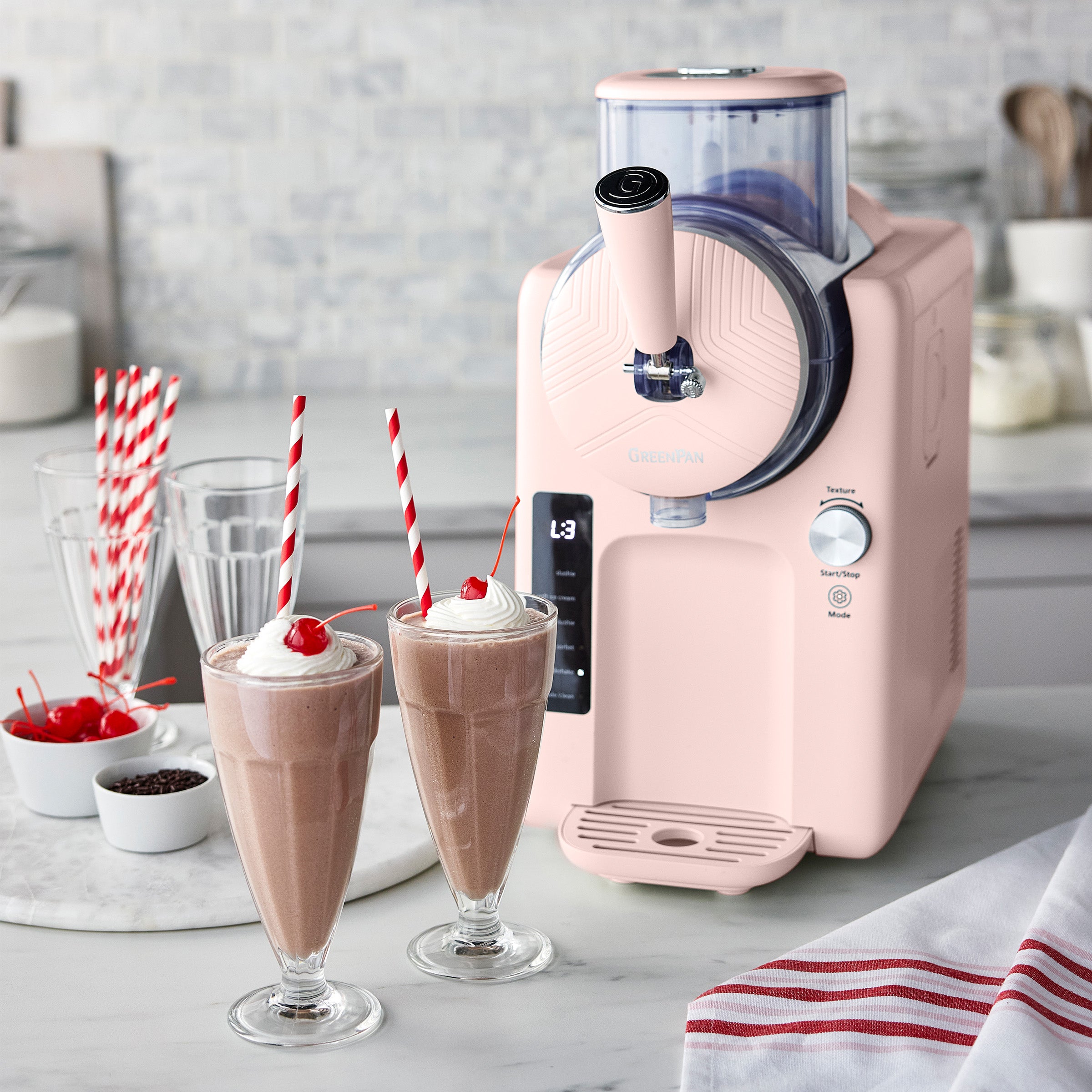 Pink ice cream machine with two chocolate milkshakes and straws on a marble countertop.