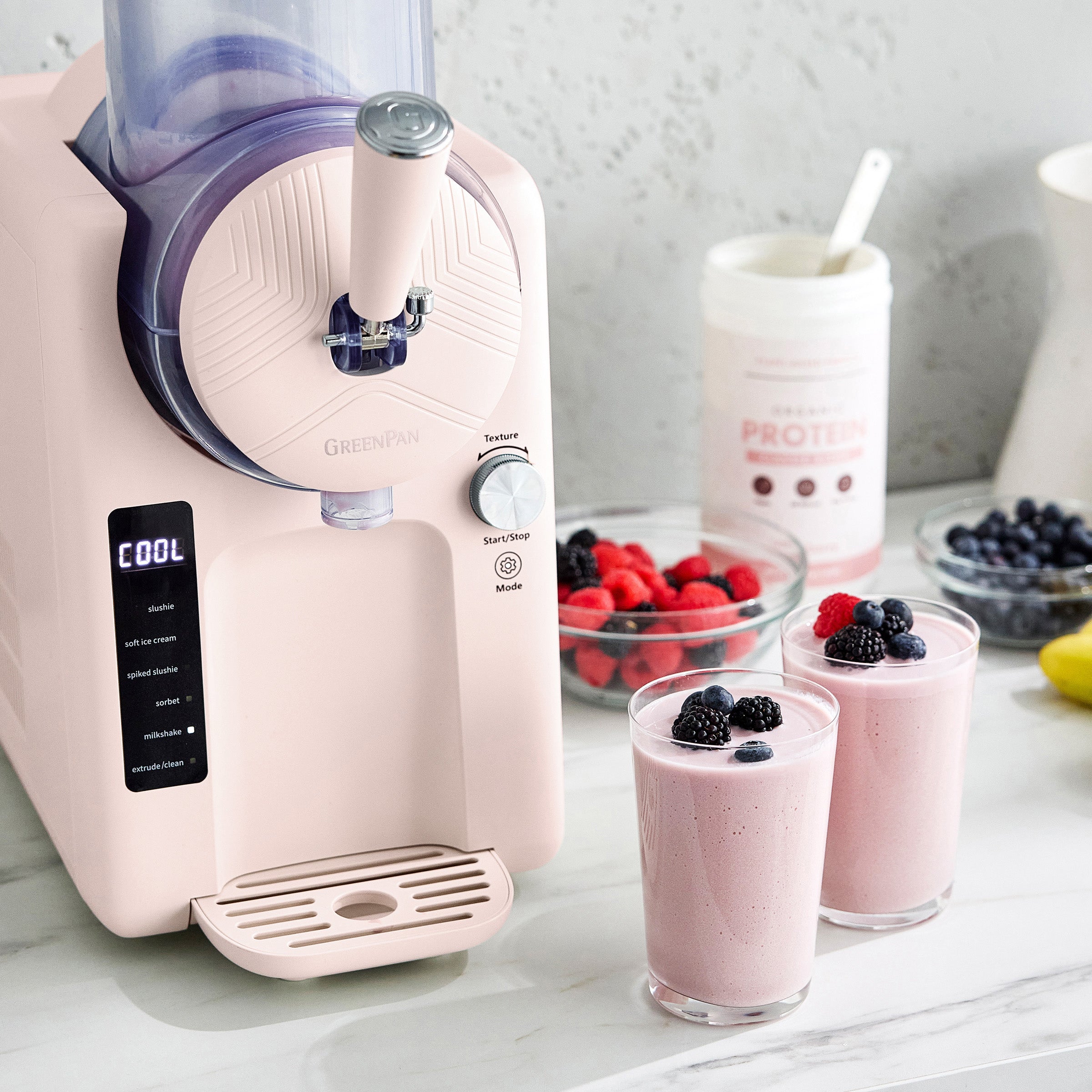 Pink kitchen appliance with smoothies and berries on a light surface