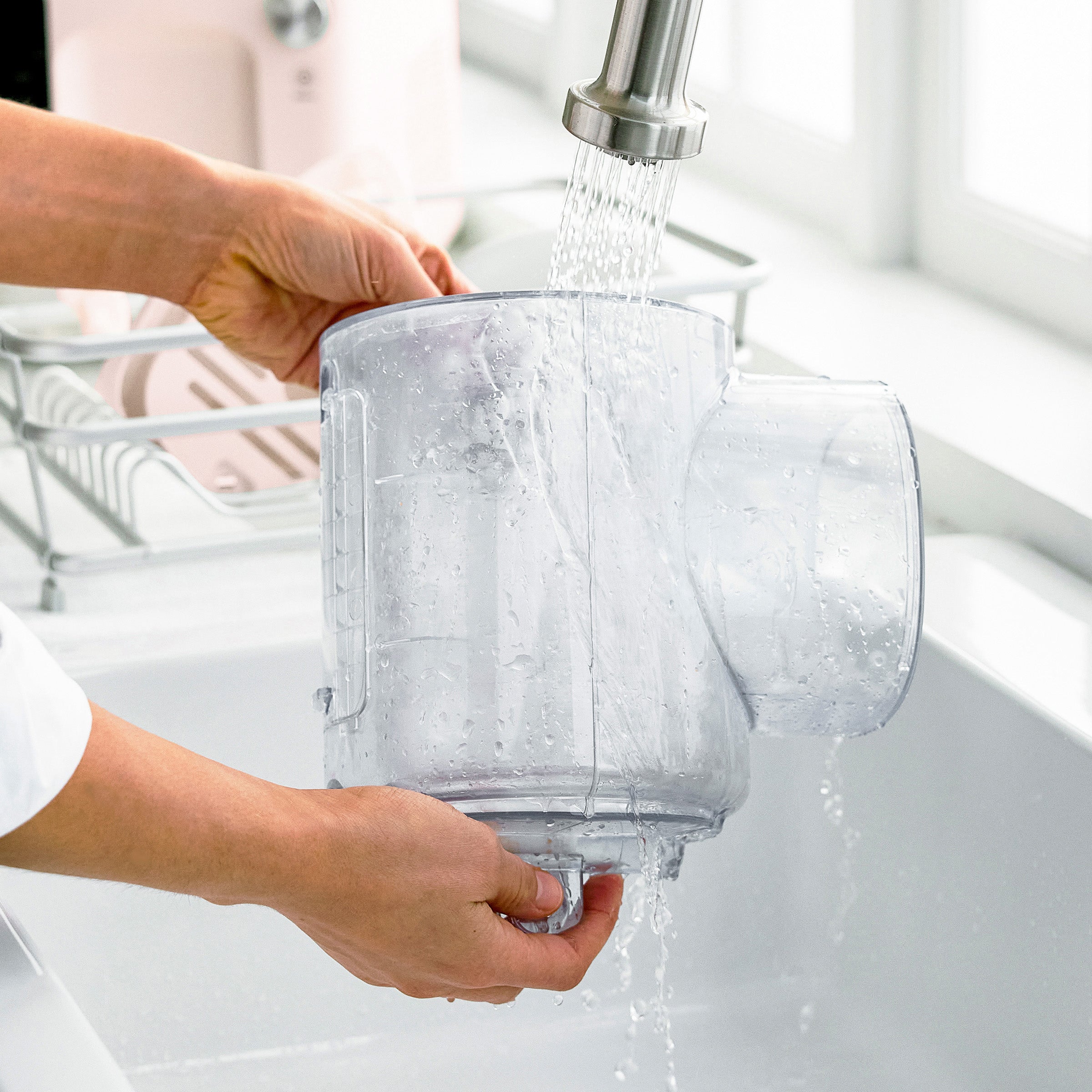 Person washing a clear container under running water from a faucet.