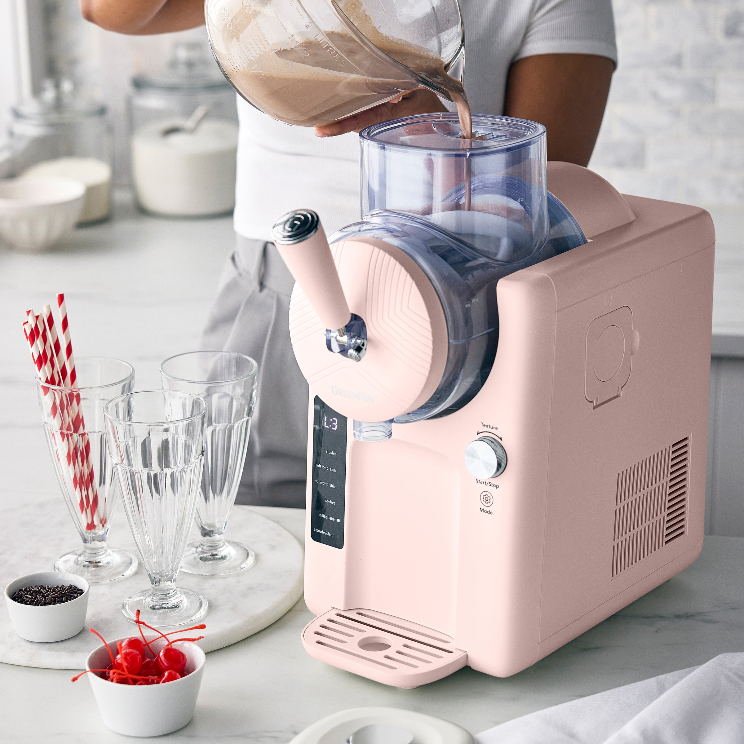Person pouring a liquid into a pink ice cream maker on a kitchen counter.