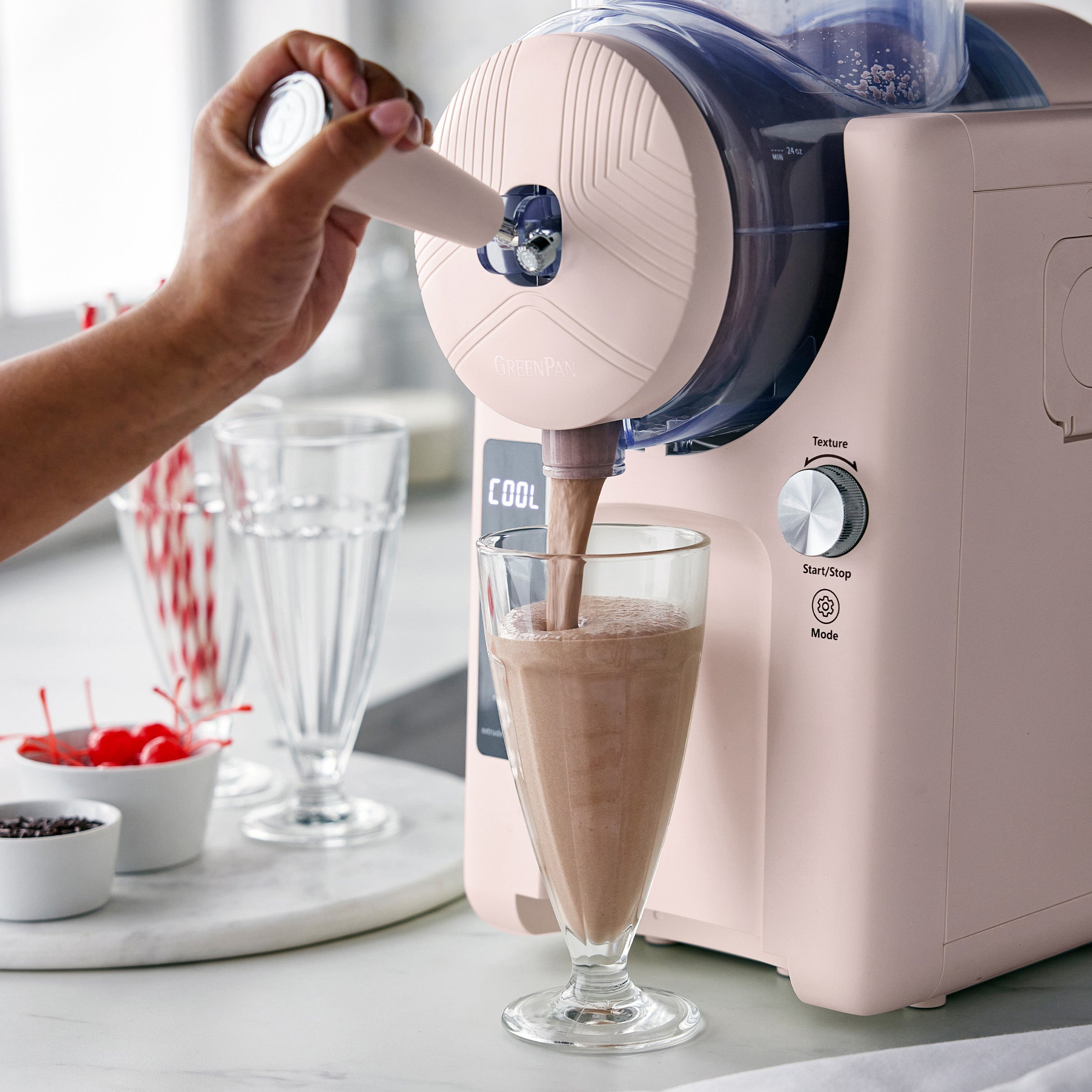 Pink kitchen appliance pouring a milkshake into a glass on a kitchen counter.