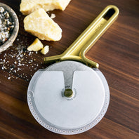 Pizza cutter with gold handle on a wooden surface with cheese and spices