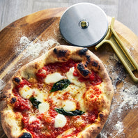 Neapolitan-style pizza with tomato sauce, mozzarella, and basil on a wooden board with a pizza cutter.