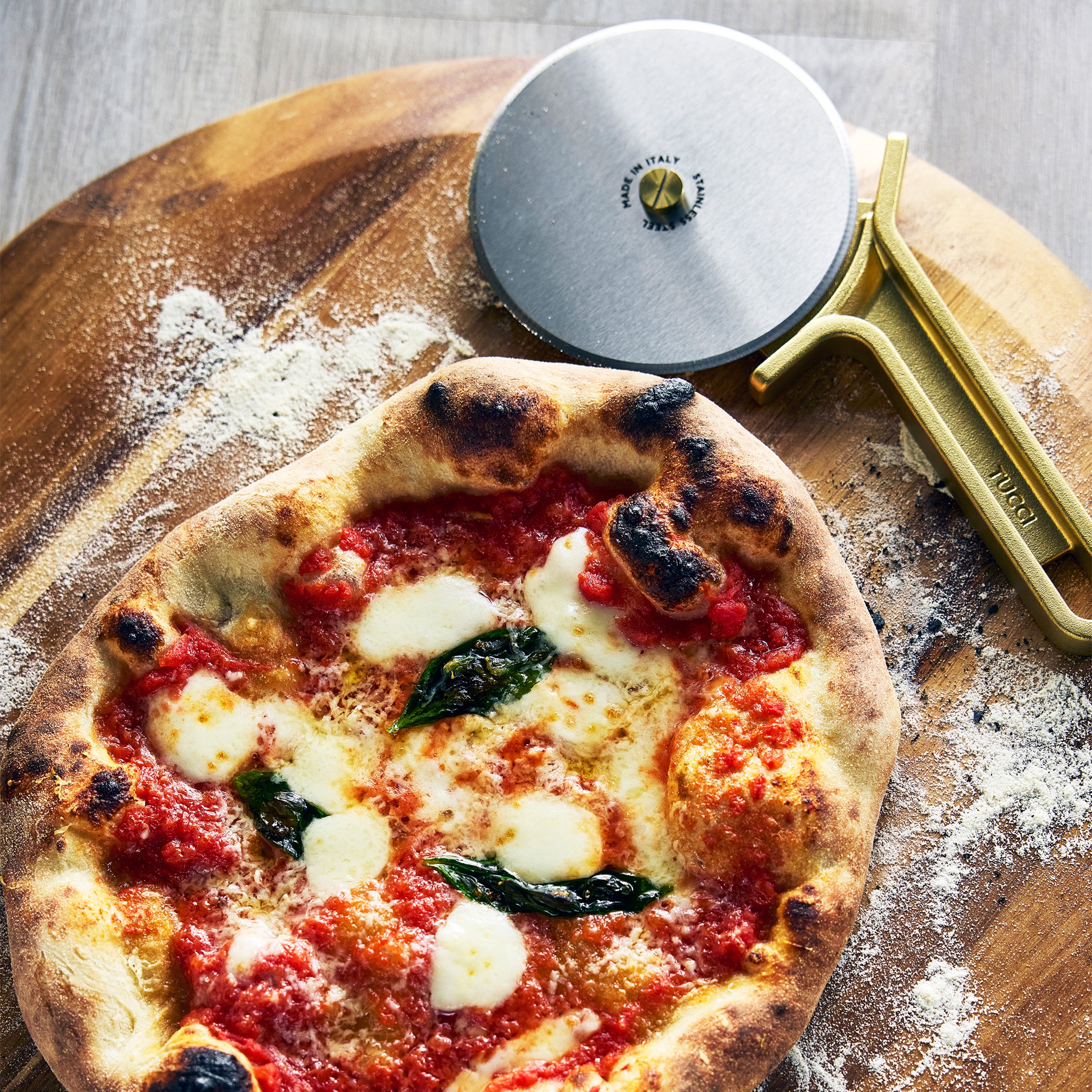 Neapolitan-style pizza with tomato sauce, mozzarella, and basil on a wooden board with a pizza cutter.