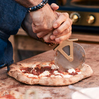 Person cutting a pizza with a pizza cutter on a wooden surface.