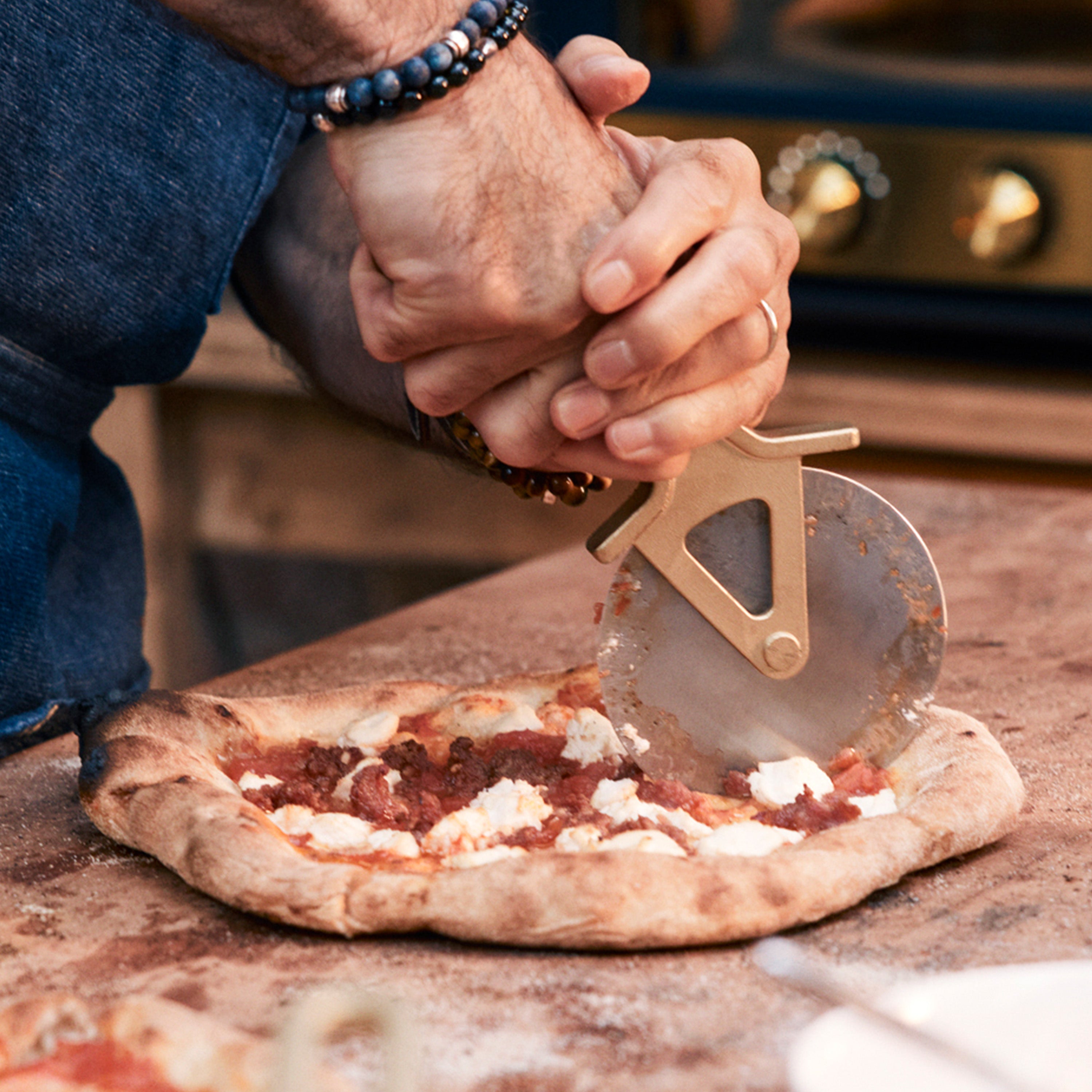 Person cutting a pizza with a pizza cutter on a wooden surface.
