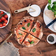 Wooden table with a pizza, tomatoes, and pizza-making tools