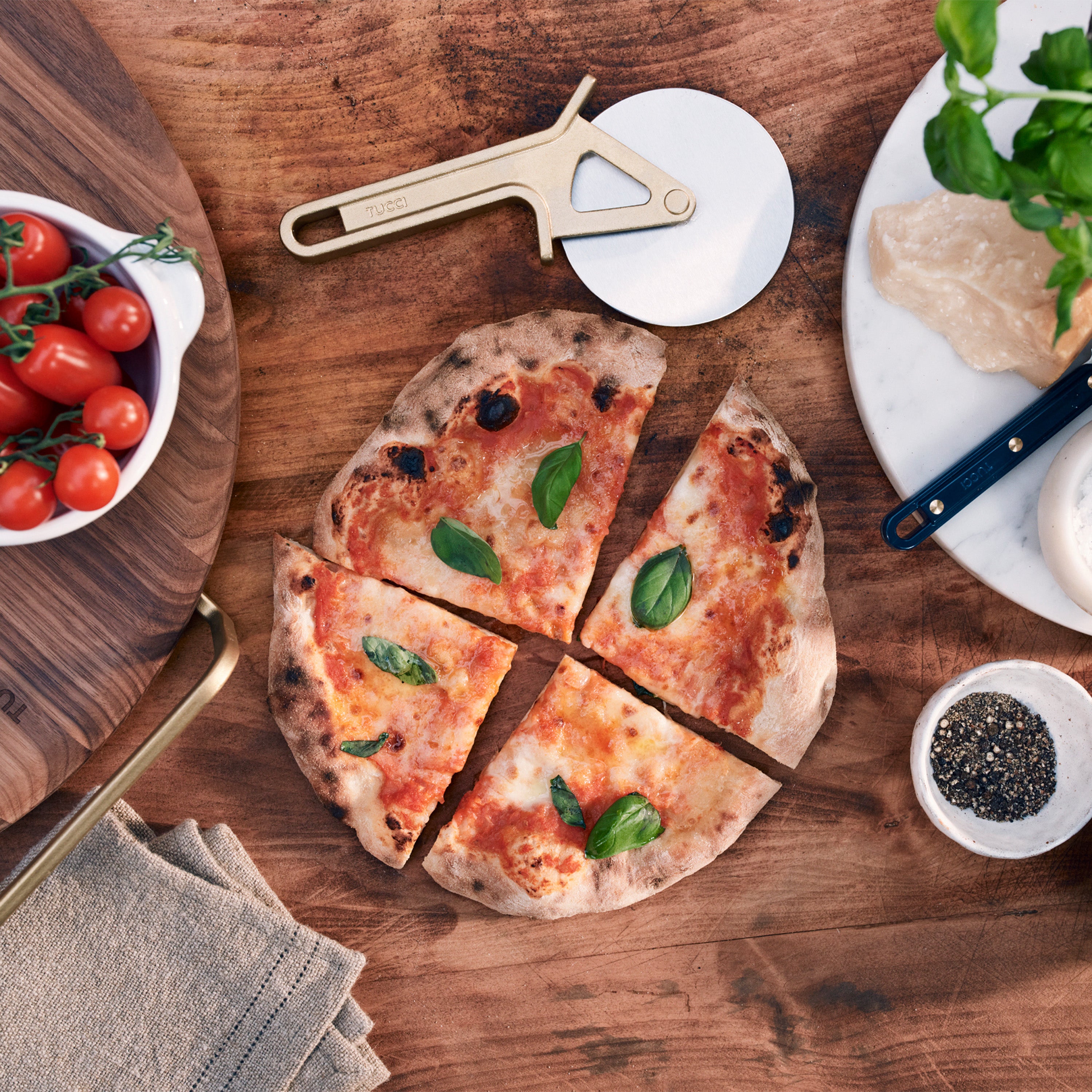 Wooden table with a pizza, tomatoes, and pizza-making tools