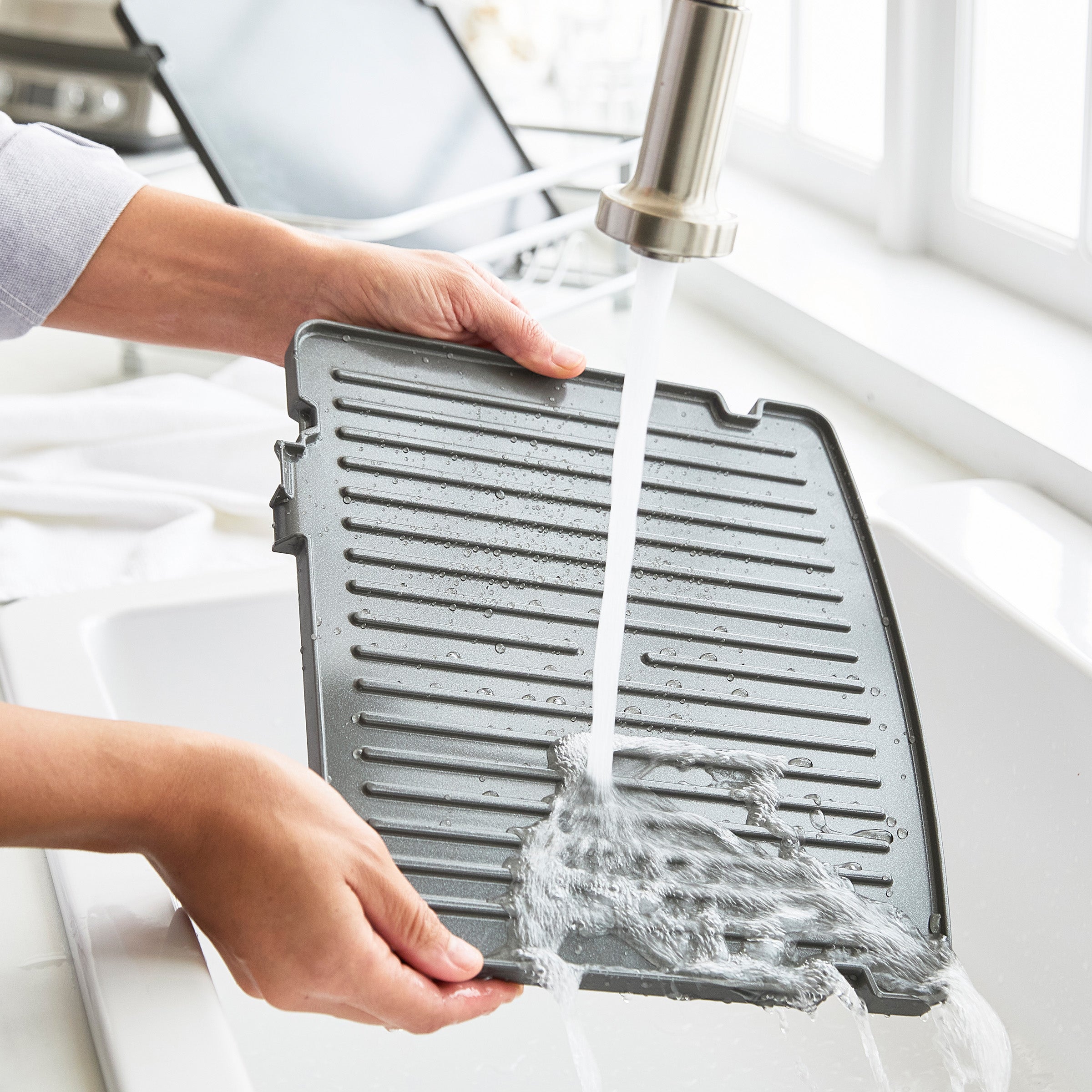 Person washing a grill pan under running water in a kitchen sink.