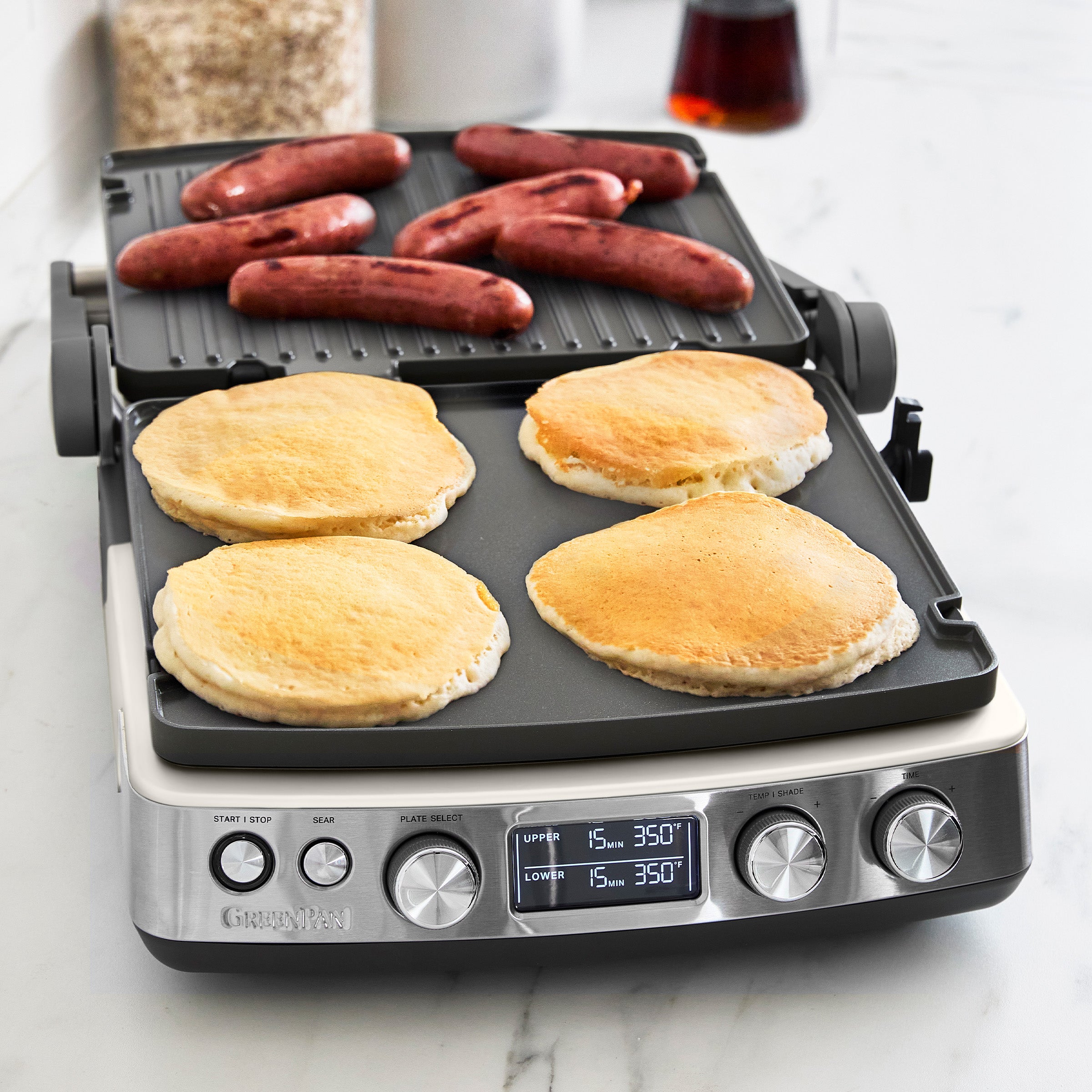 Multifunctional cooking appliance with pancakes and sausages on a marble countertop