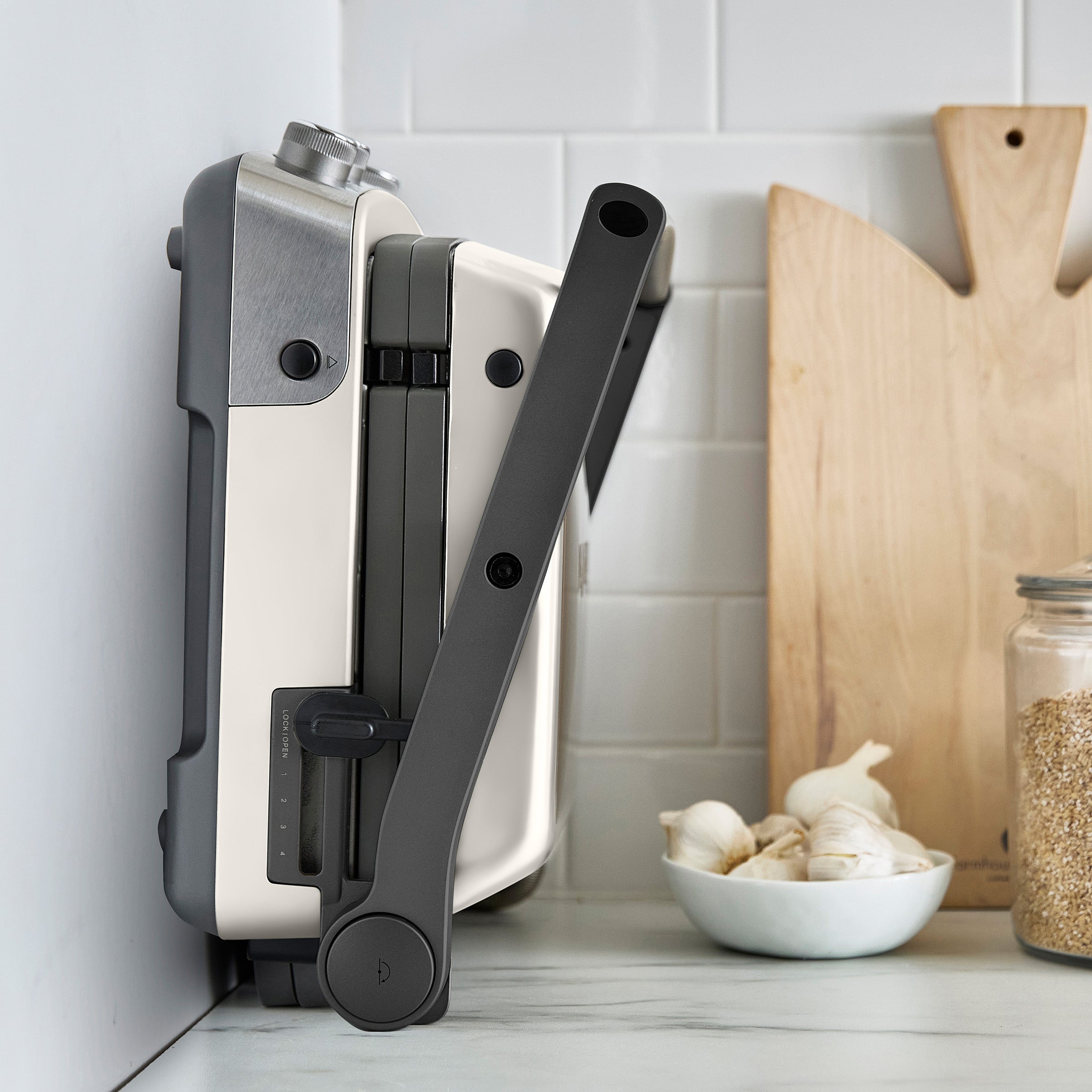 Foldable kitchen tool on a kitchen counter with a cutting board and ingredients in the background.