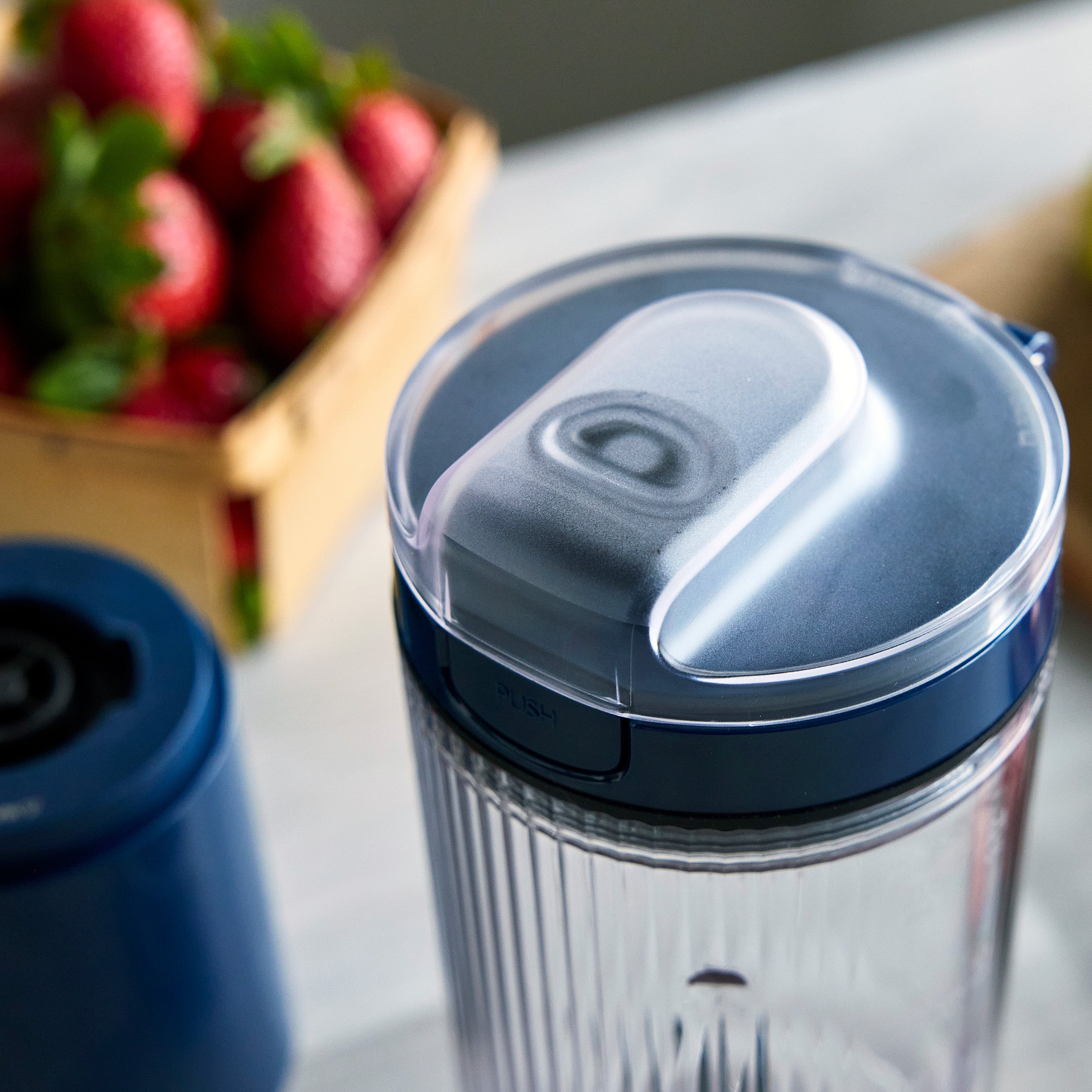 Clear tumbler with blue lid on a surface with strawberries in the background