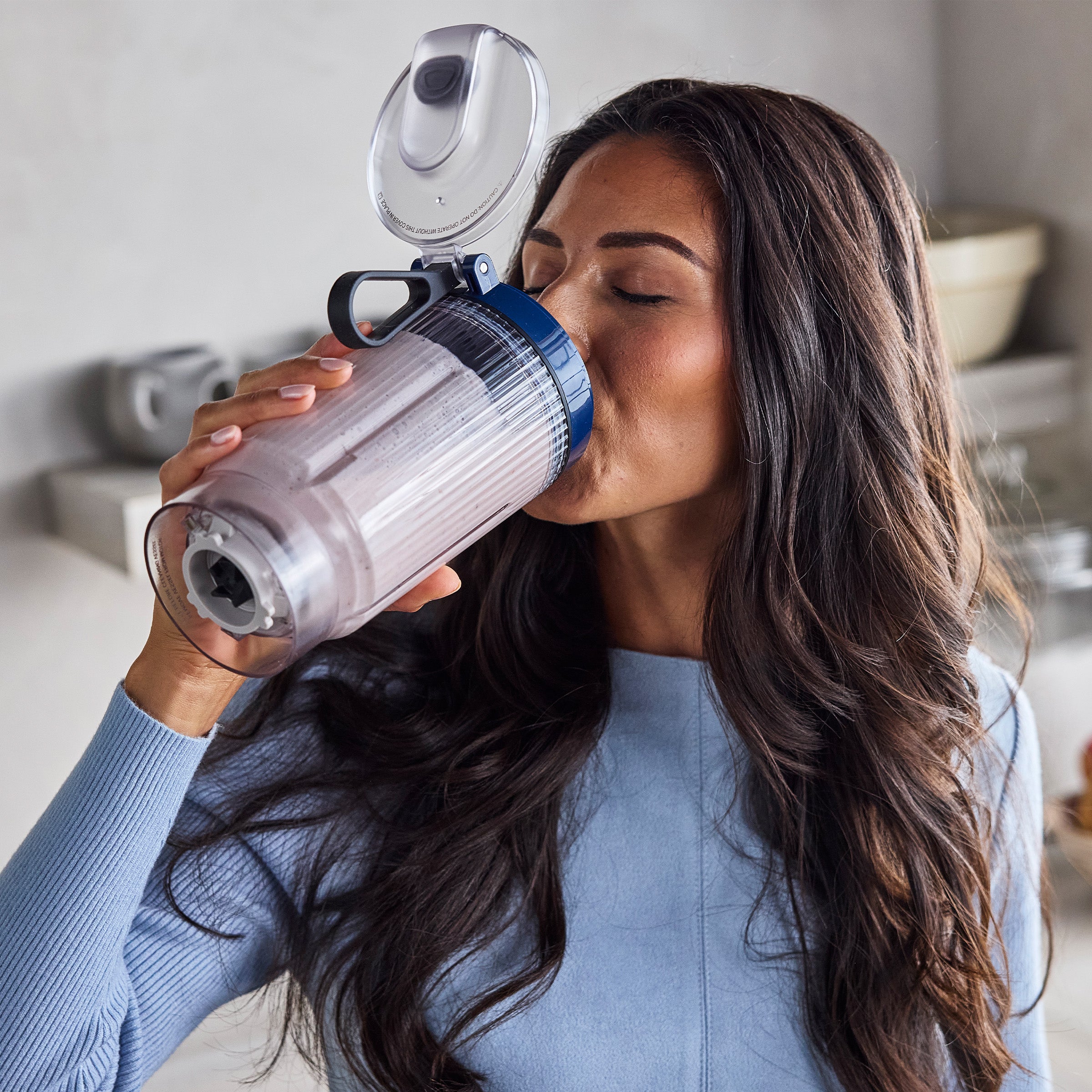 Woman drinking from a portable blender cup in a kitchen setting