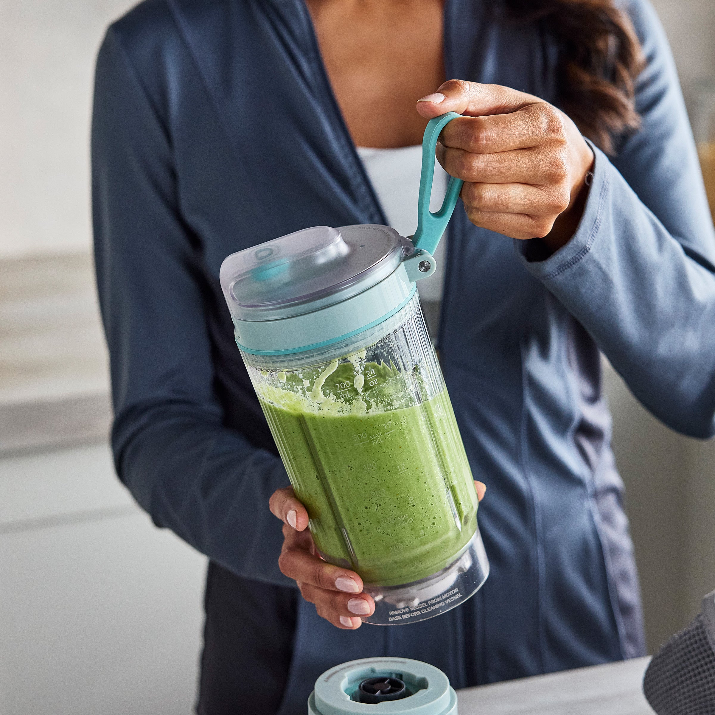 Person holding a green smoothie in a portable blender with a blue handle.