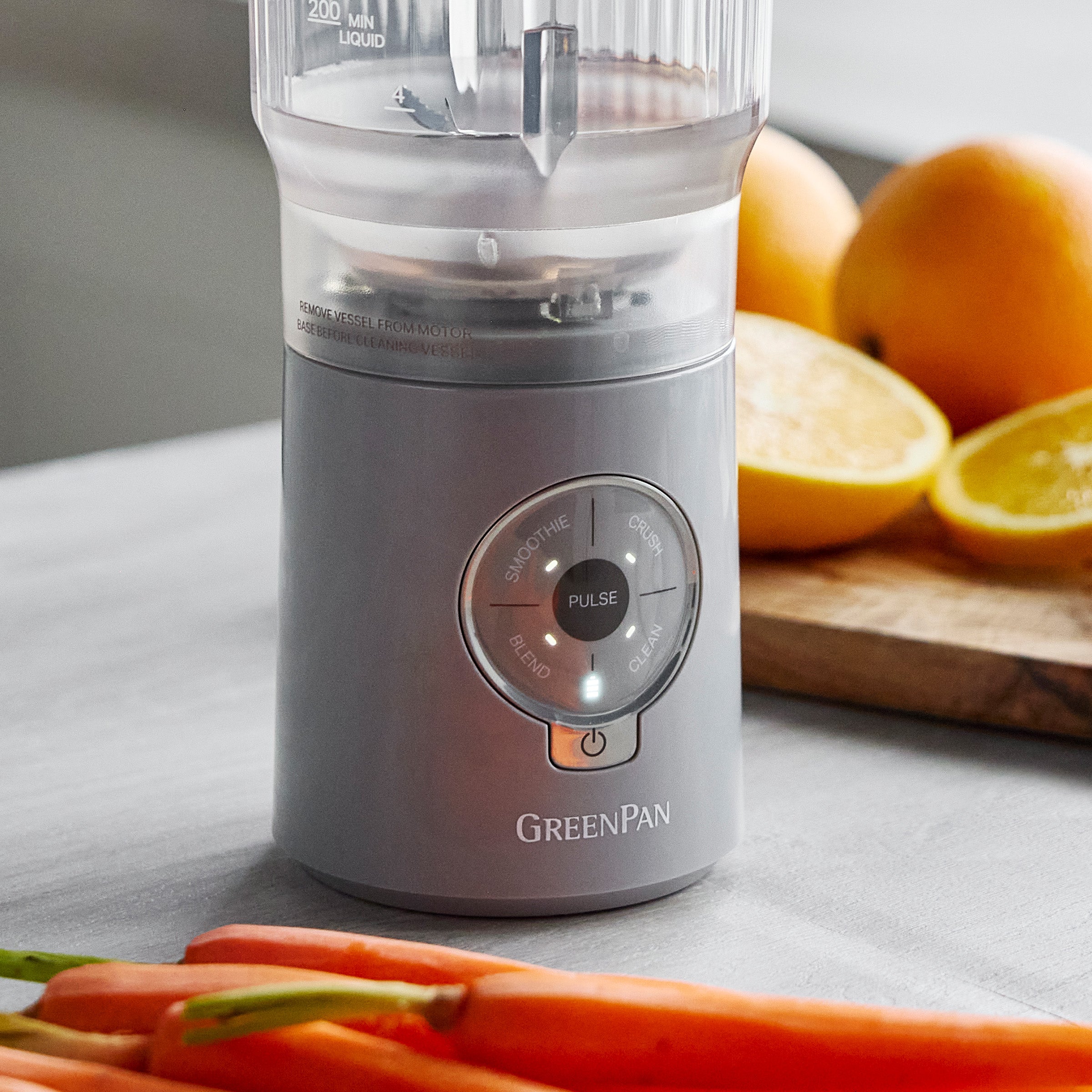 Gray blender with 'GreenPan' branding on a kitchen counter with fruits and vegetables.