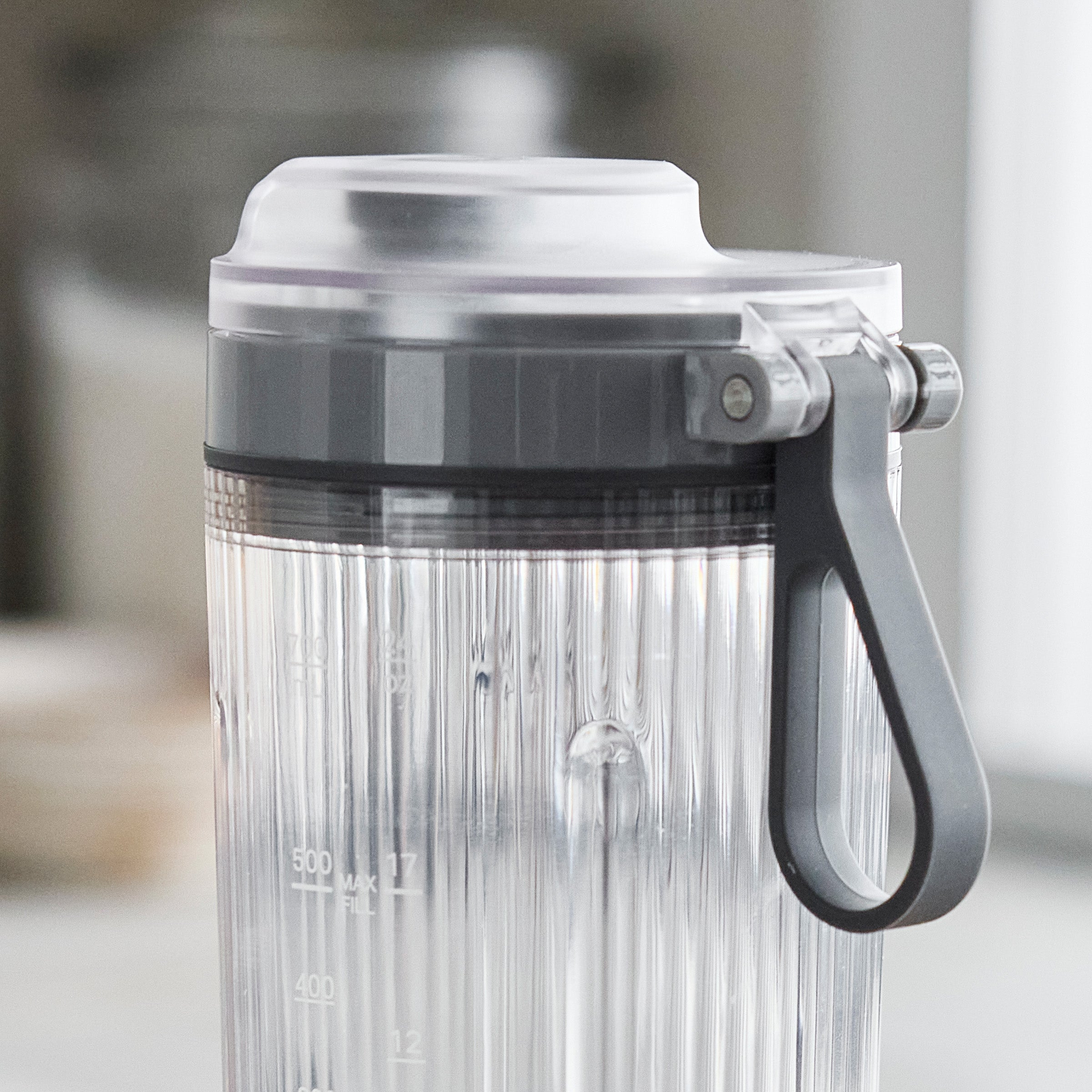 Portable blender with a gray handle and lid on a blurred background