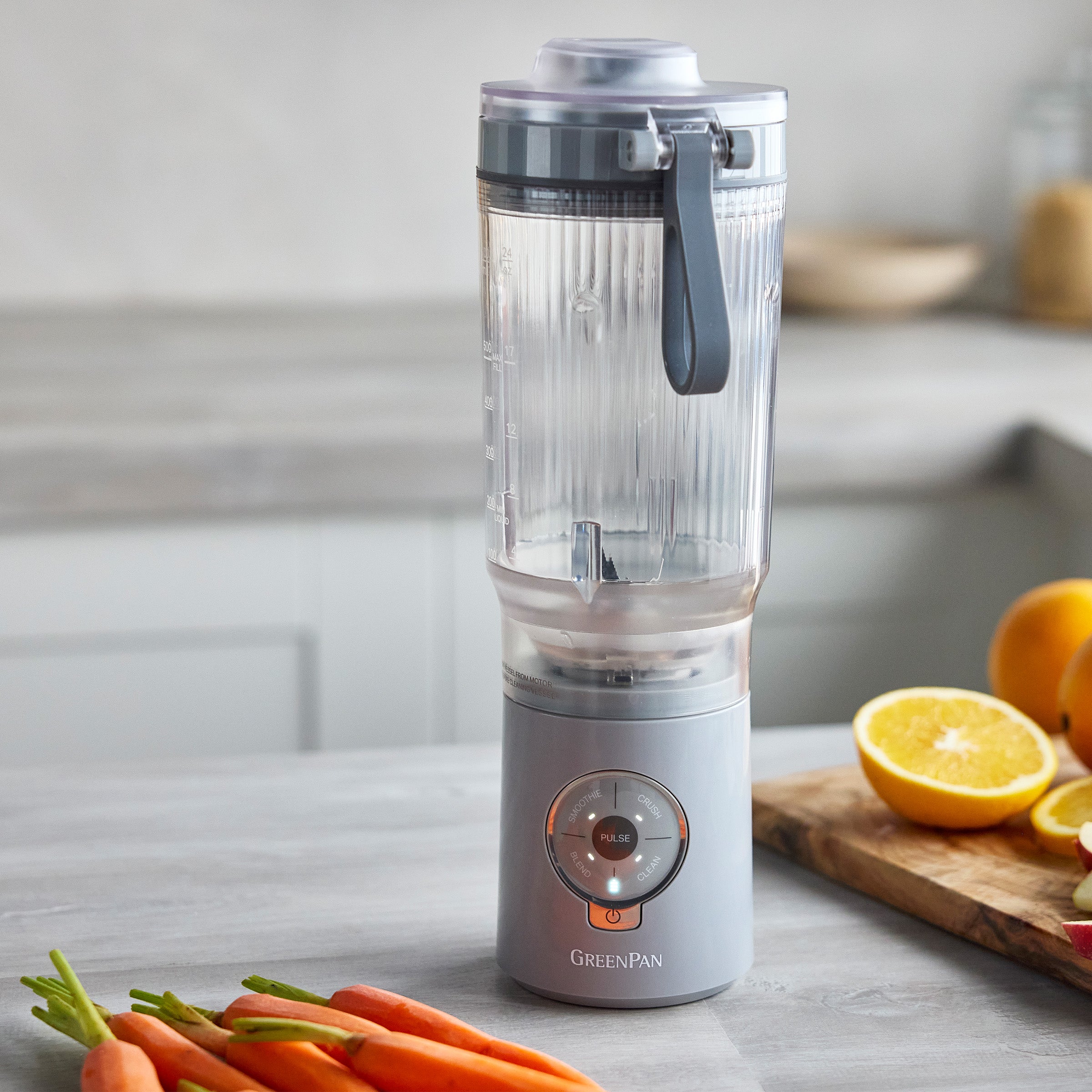 Portable blender on a kitchen counter with carrots and citrus in the background