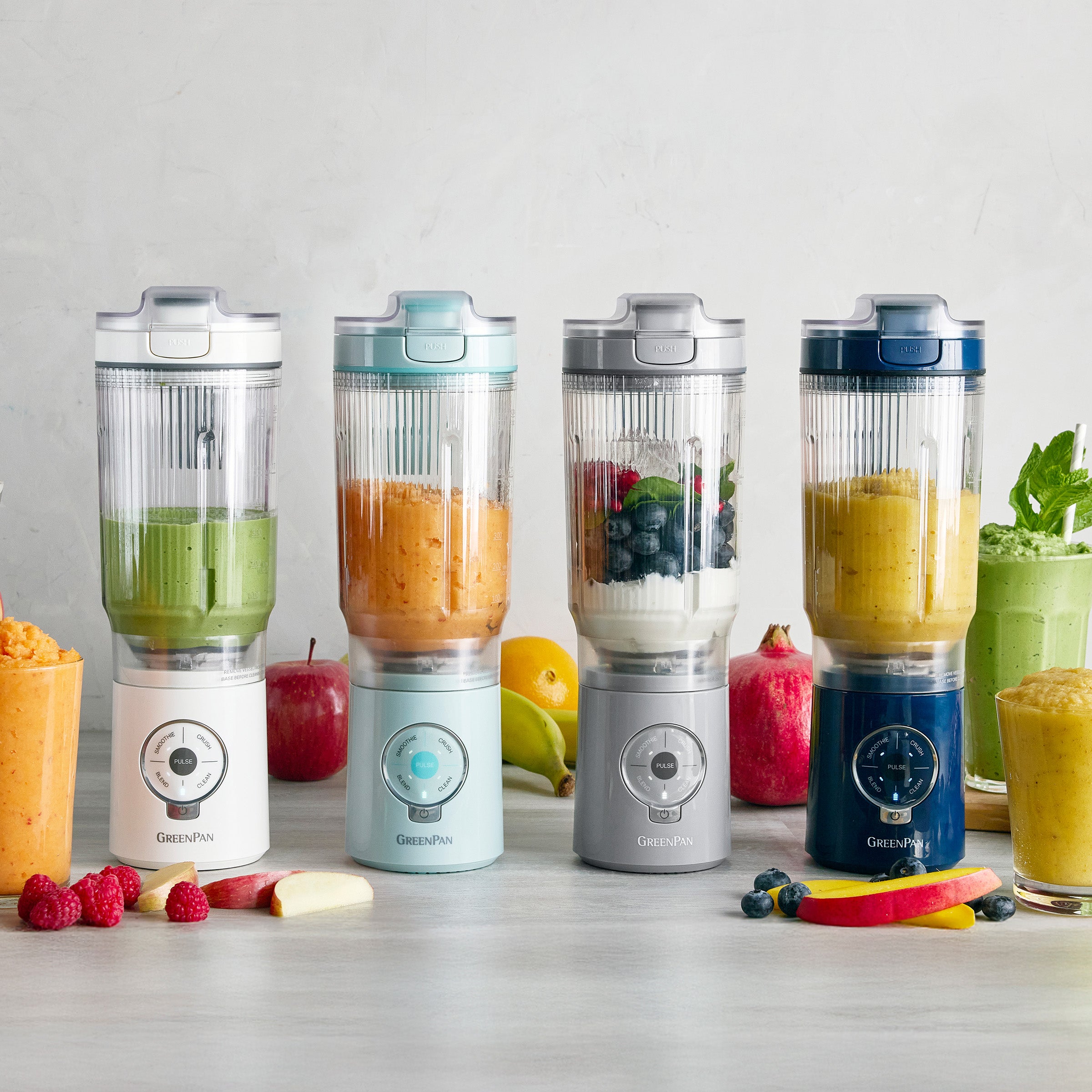 Four portable blenders with different colored drinks on a light surface.